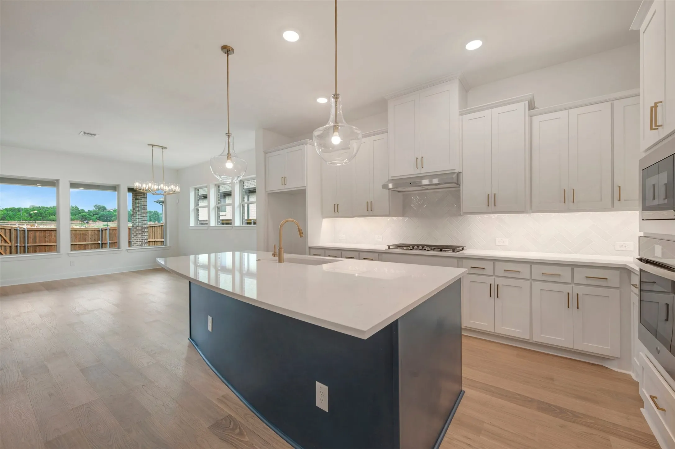 The kitchen features a spacious island with a white countertop and a dark base, pendant lighting, and white cabinetry with gold hardware