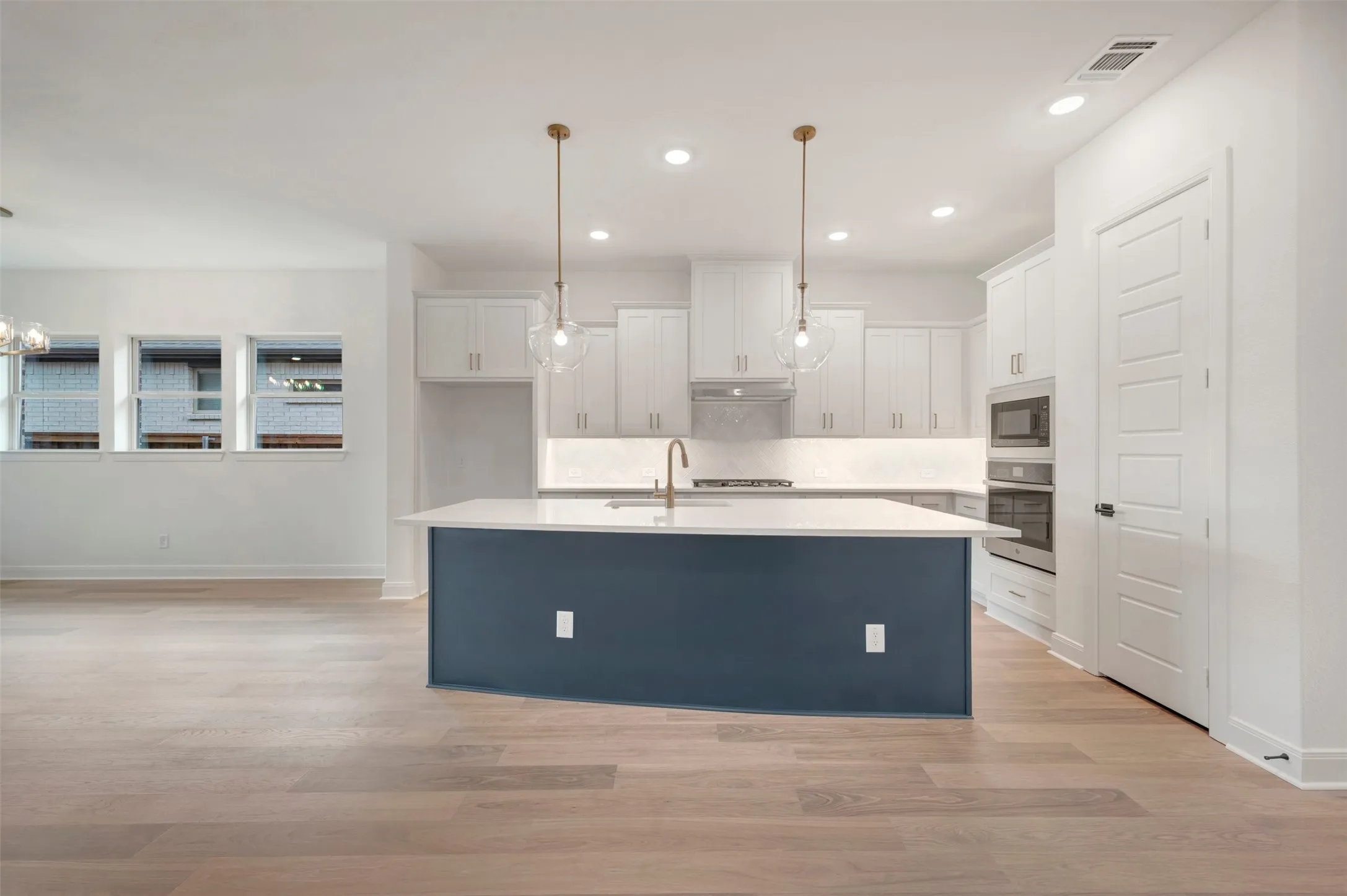 The kitchen features white cabinetry, a large kitchen island with a dark base and light countertop, and modern pendant lighting