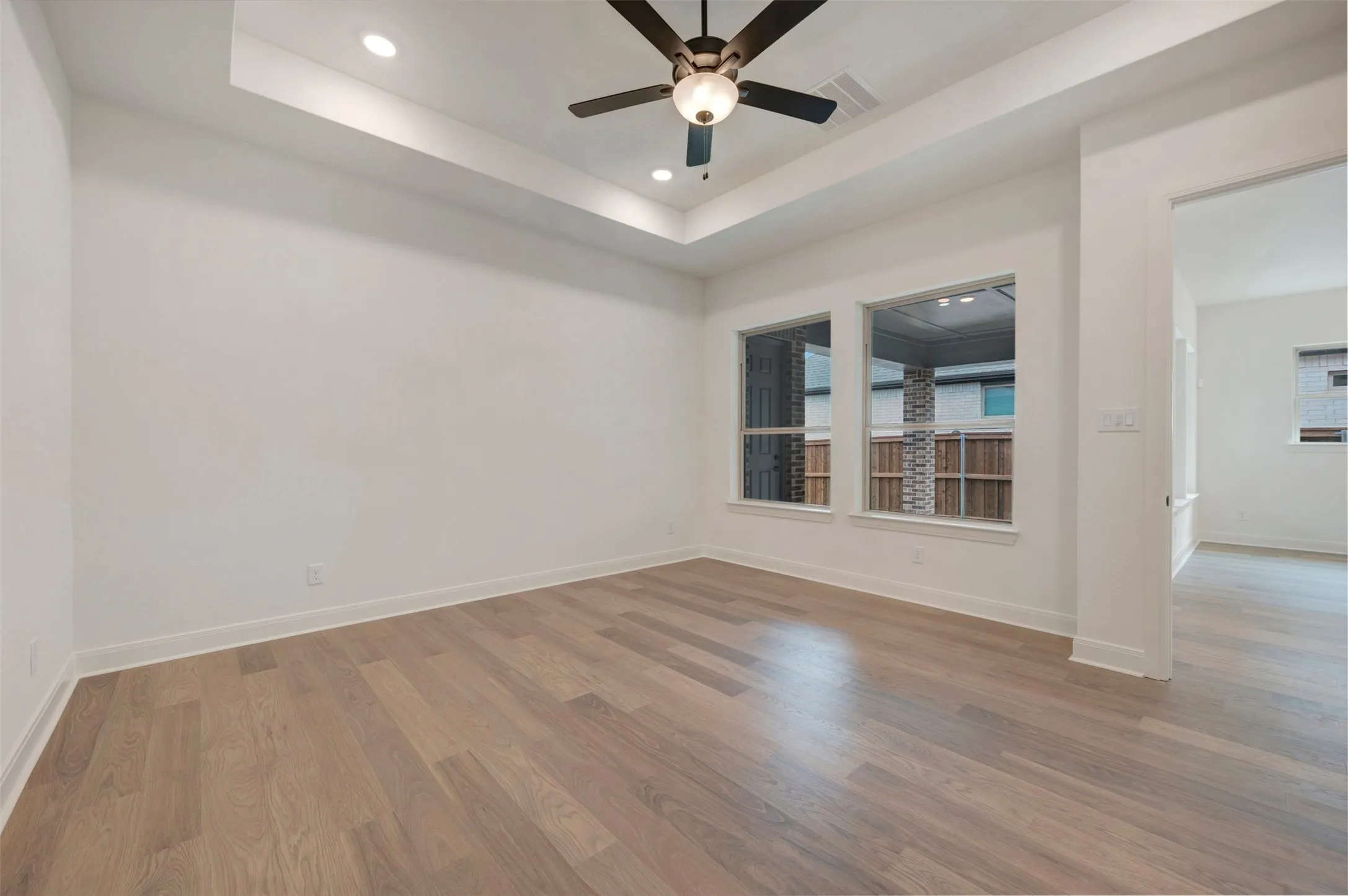 Room featuring light wood flooring, white walls, two windows, and a ceiling fan with integrated lighting