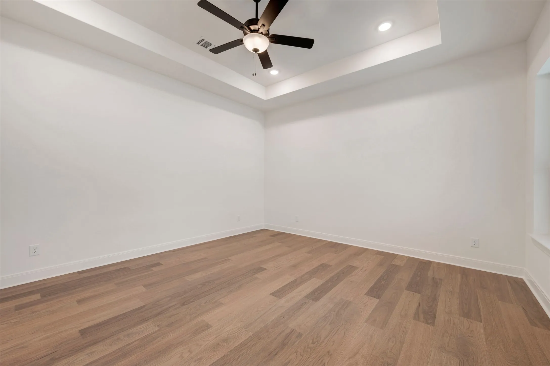 This room features light-colored walls, wood flooring, and a ceiling fan