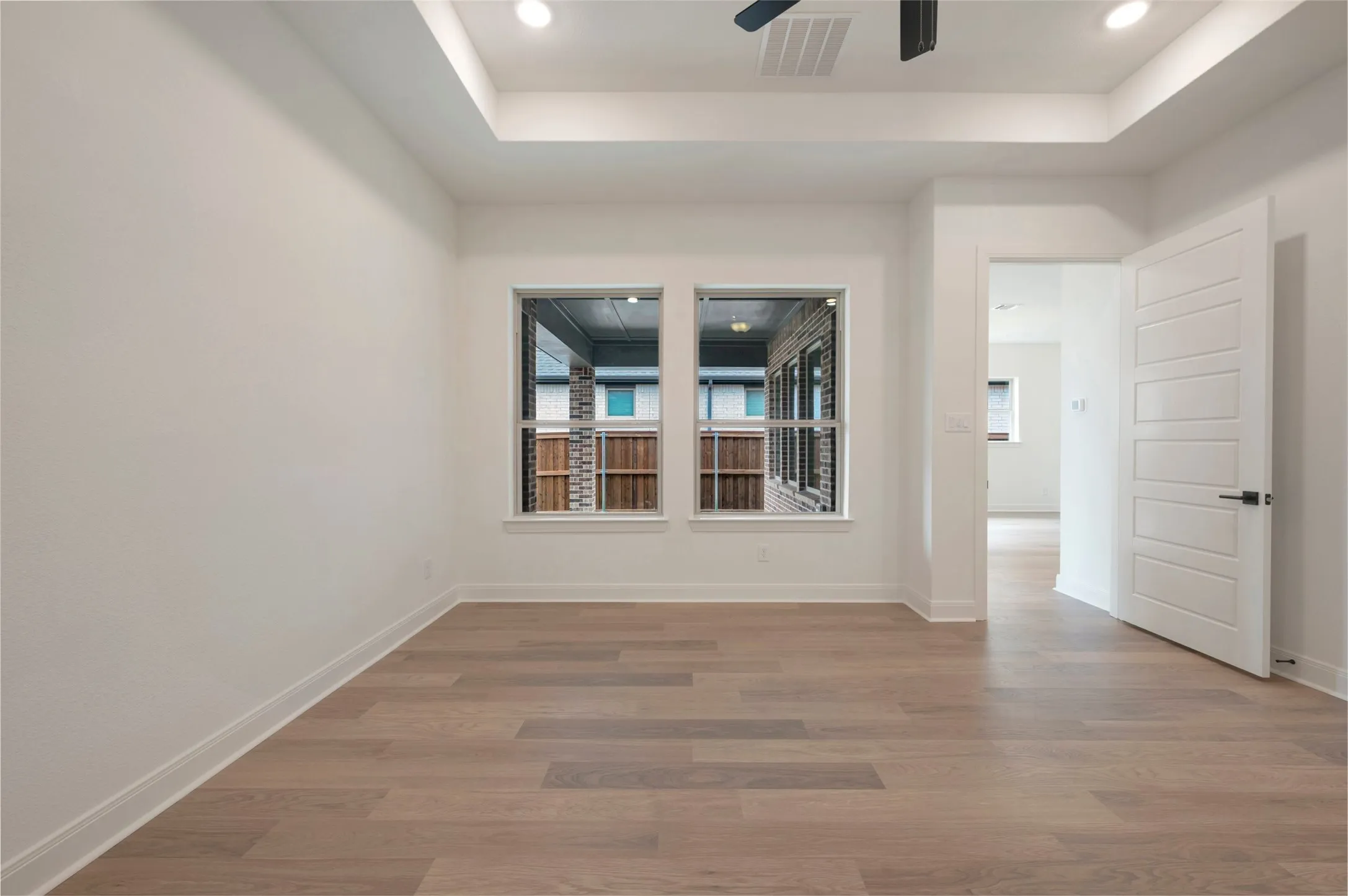 This room features light-colored hardwood flooring, white walls, and a tray ceiling with recessed lighting