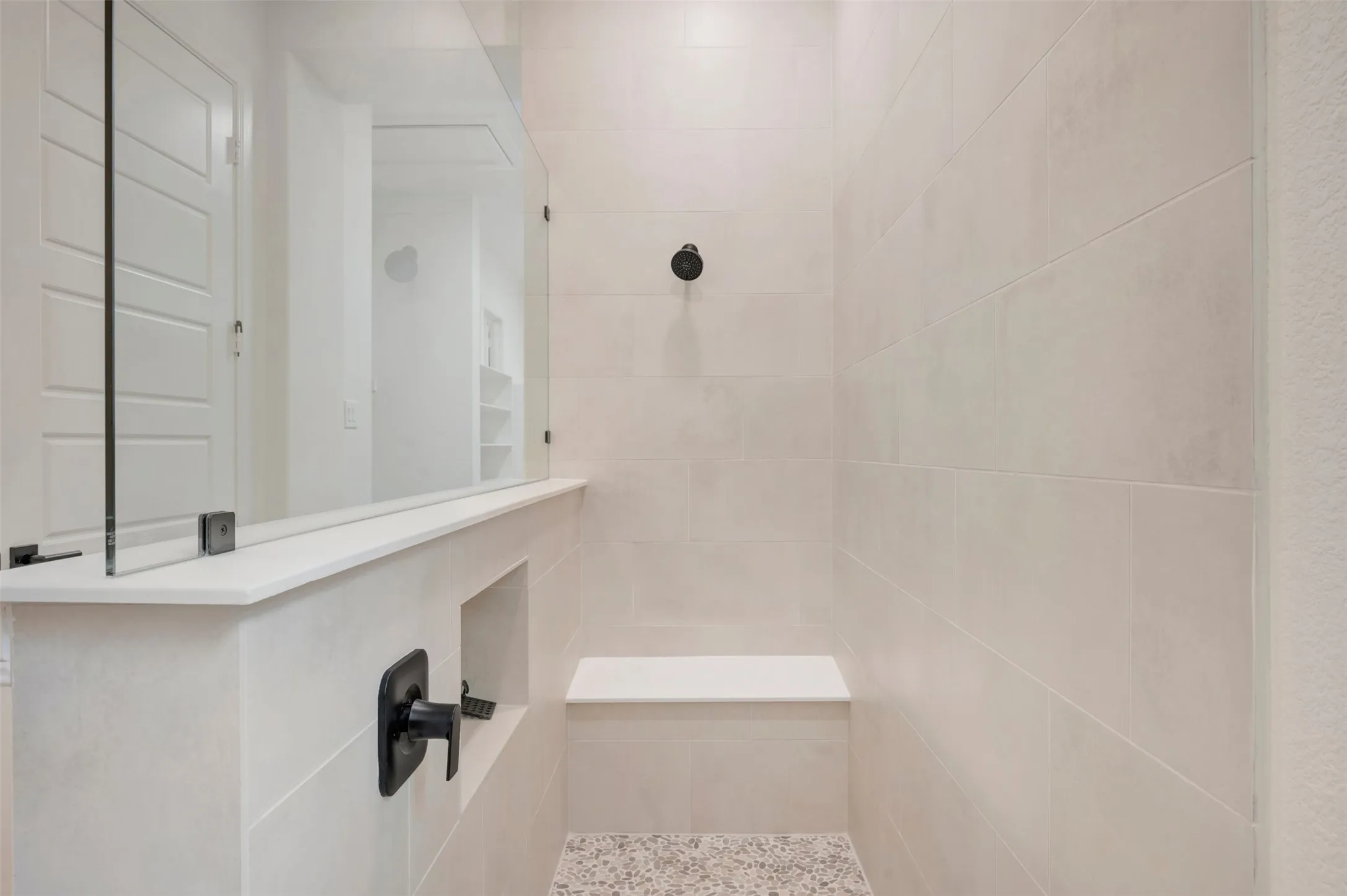 The shower features light-colored tile walls, a built-in bench, and a dark-toned shower head