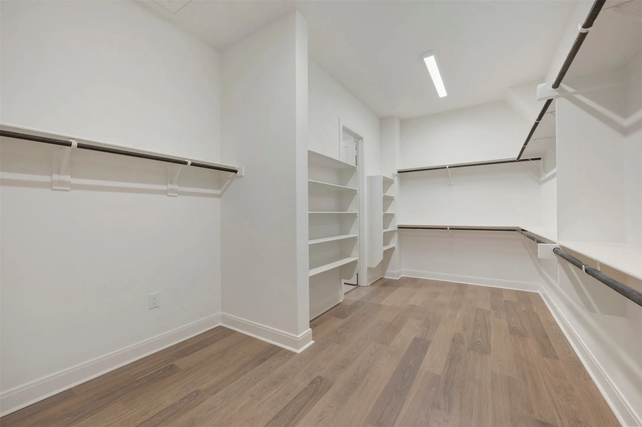 Spacious closet featuring light wood-look flooring, white walls, and extensive shelving and hanging rods for ample storage