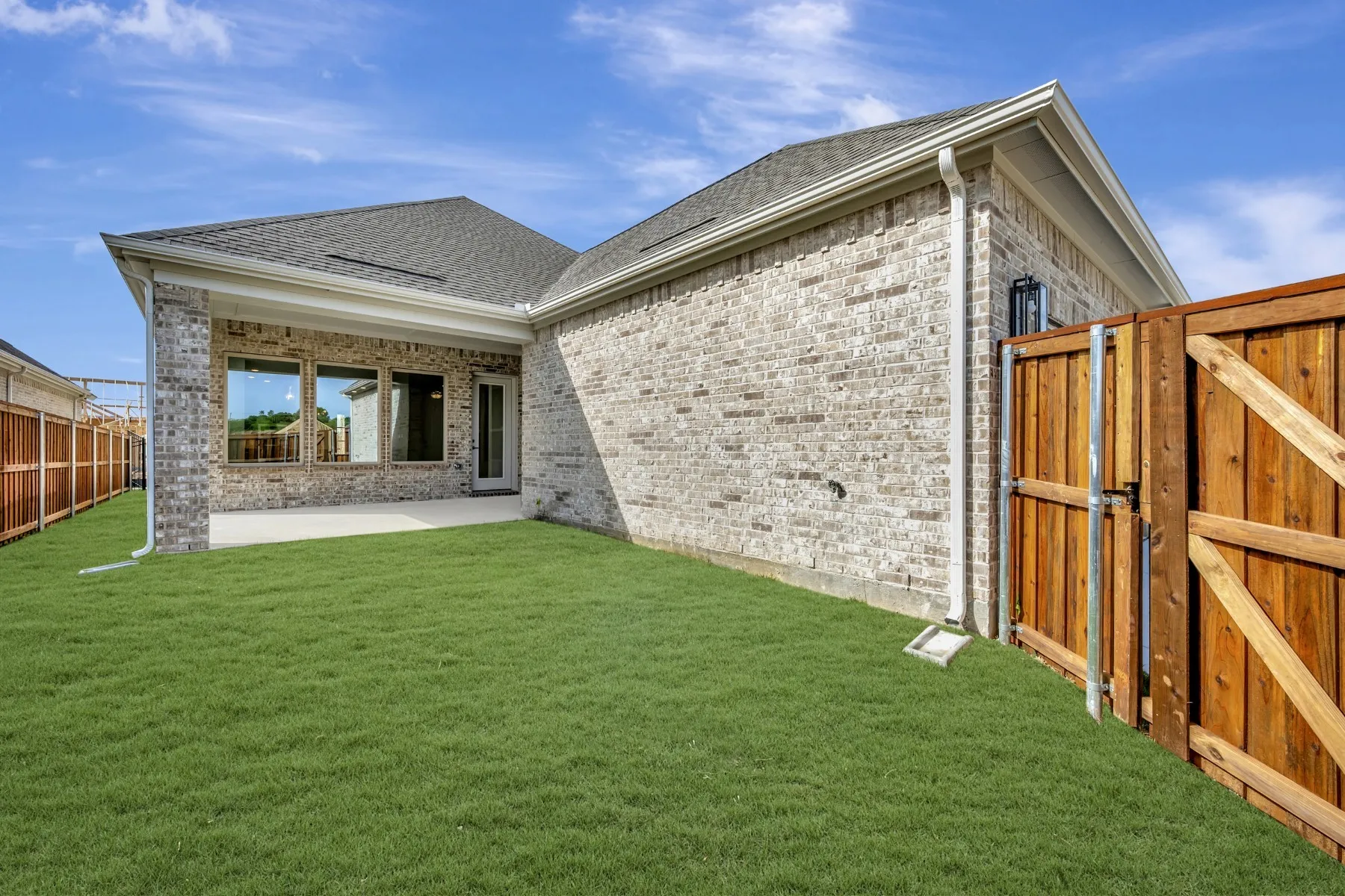Back of property with a patio area, a shingled roof, brick siding, and a gate