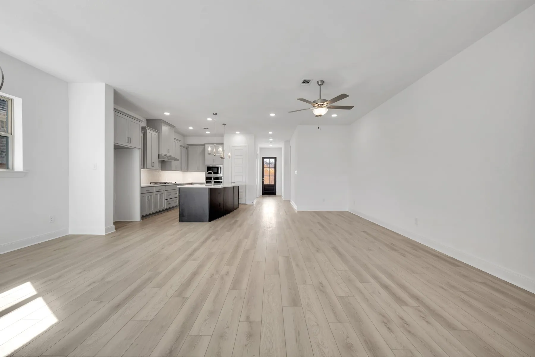 Unfurnished living room with a ceiling fan, light wood-style flooring, and hanging lights
