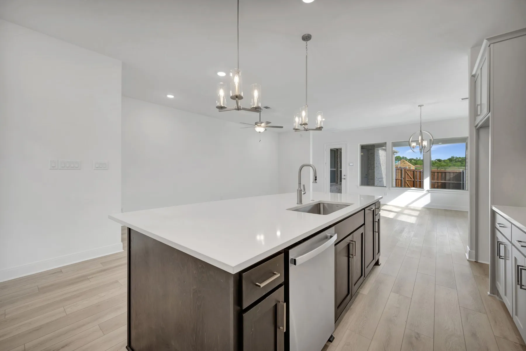 Kitchen with hanging lights, stainless steel dishwasher, light wood-style flooring, and a center island with sink