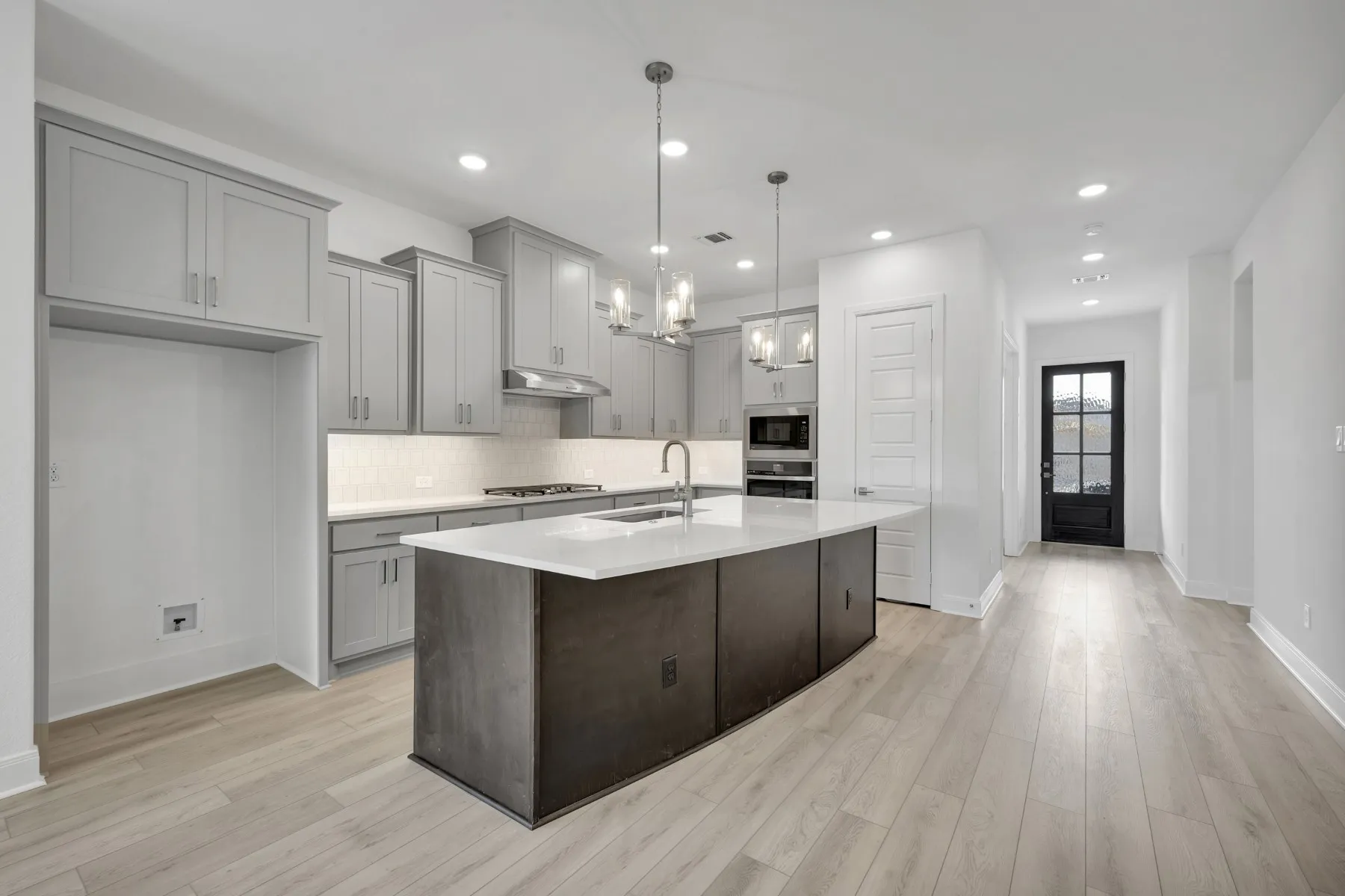 Kitchen featuring hanging lights, a kitchen island with sink, gray cabinetry, light wood-type flooring, and light stone counters