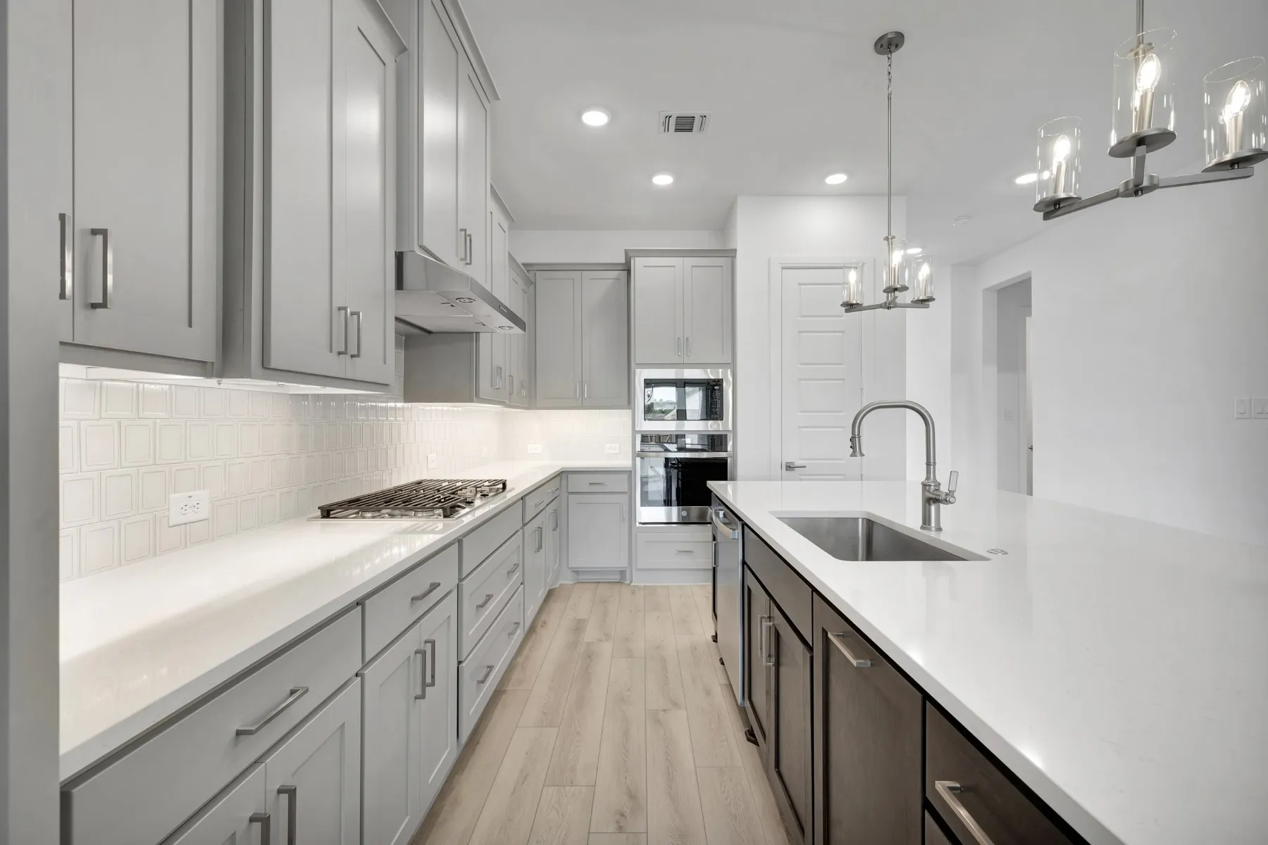 Kitchen featuring stainless steel appliances, light wood-type flooring, suspended lighting, tasteful backsplash, and light stone counters