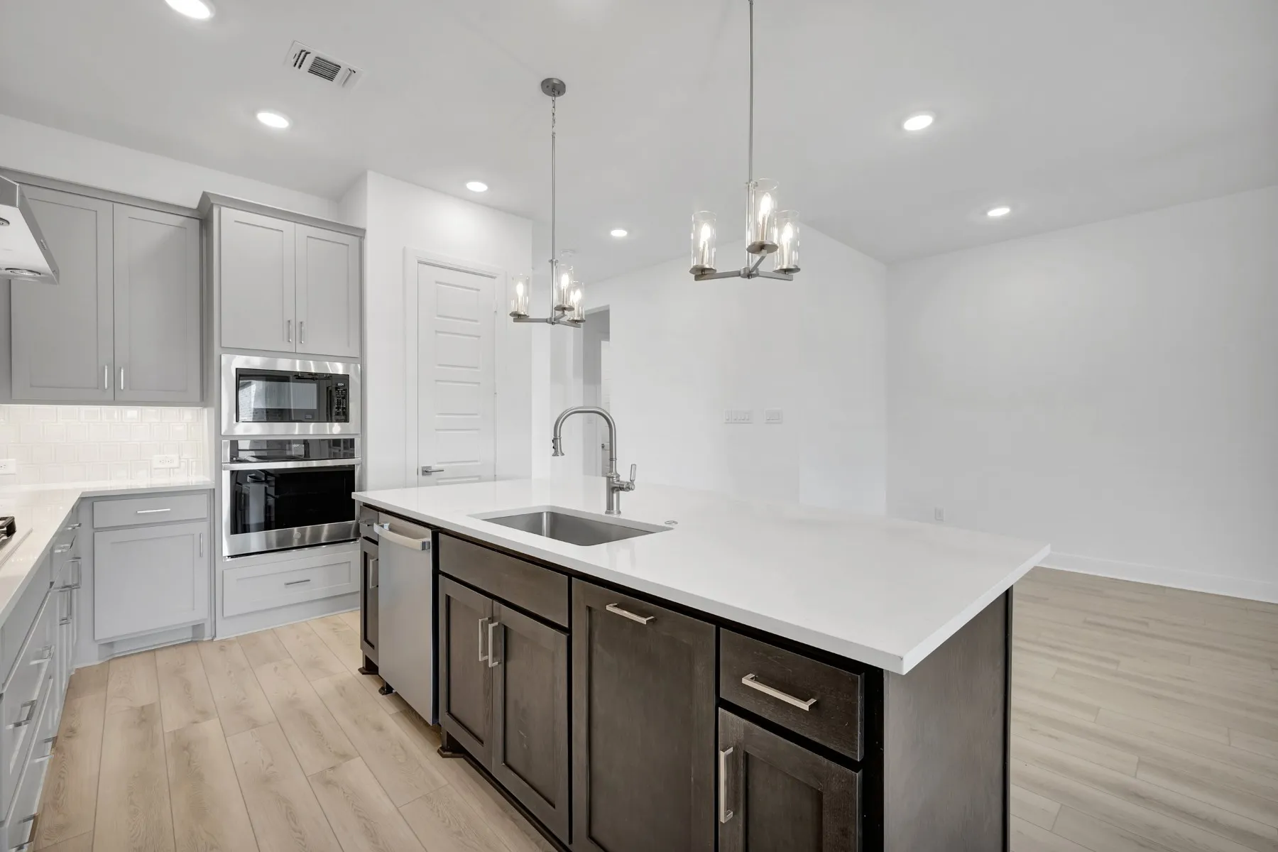 Kitchen featuring light wood-style floors, stainless steel appliances, an island with sink, suspended lighting, and backsplash