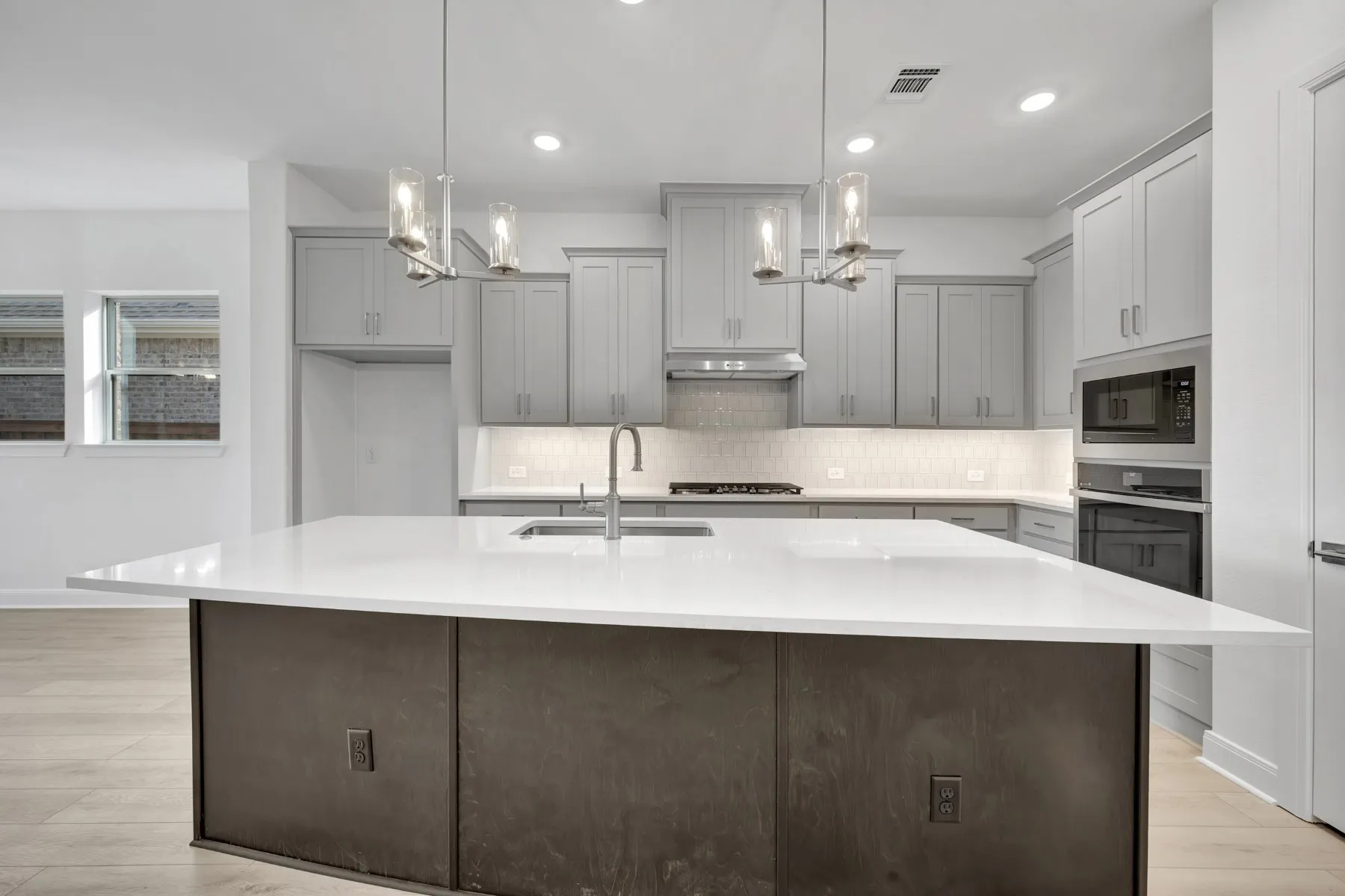 Kitchen with an island with sink, gray cabinets, light wood finished floors, and light stone counters