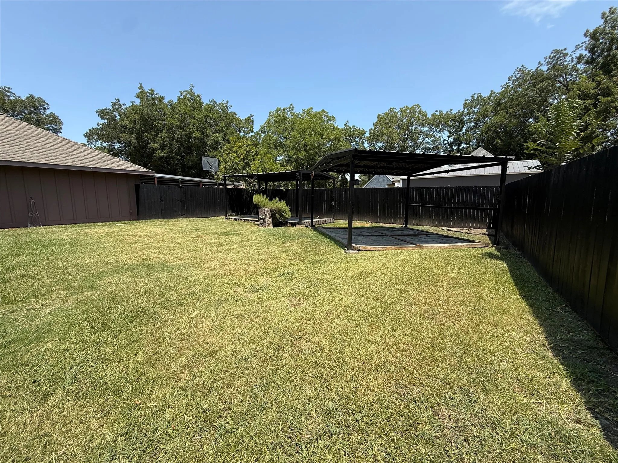 Expansive backyard featuring a large grass area, wood privacy fencing, and a covered patio structure