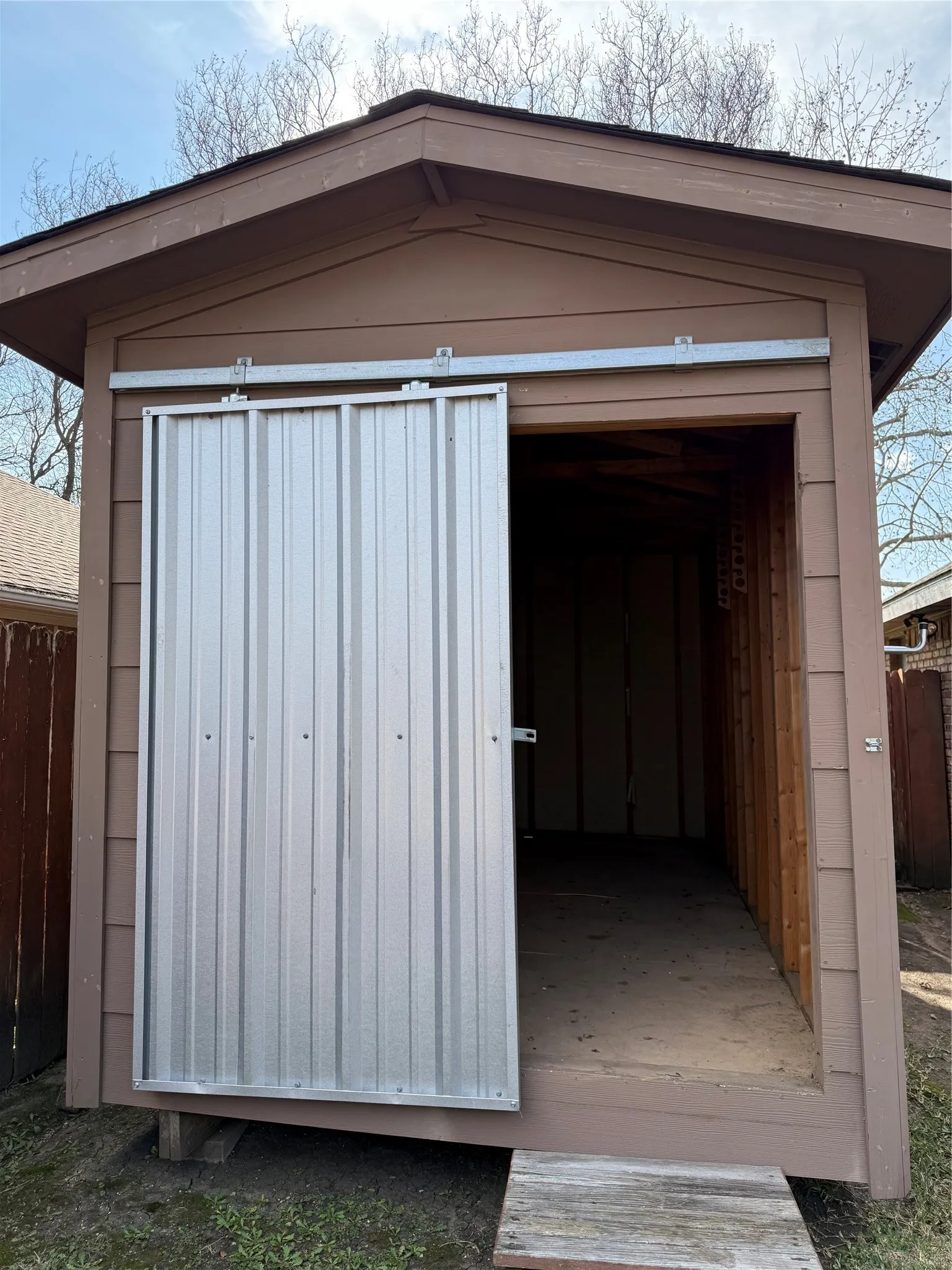Brown-painted wood-sided shed featuring a corrugated metal sliding door and a built-in wooden ramp