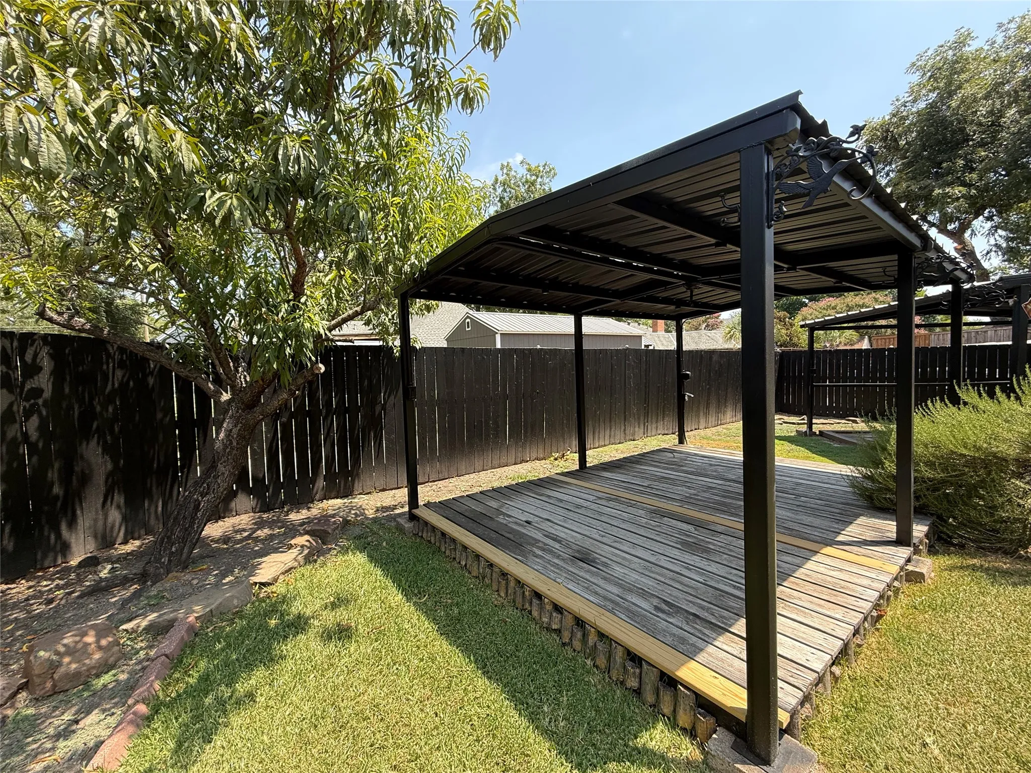 Expansive backyard featuring a covered outdoor living structure, a wood-plank deck, and a mature tree
