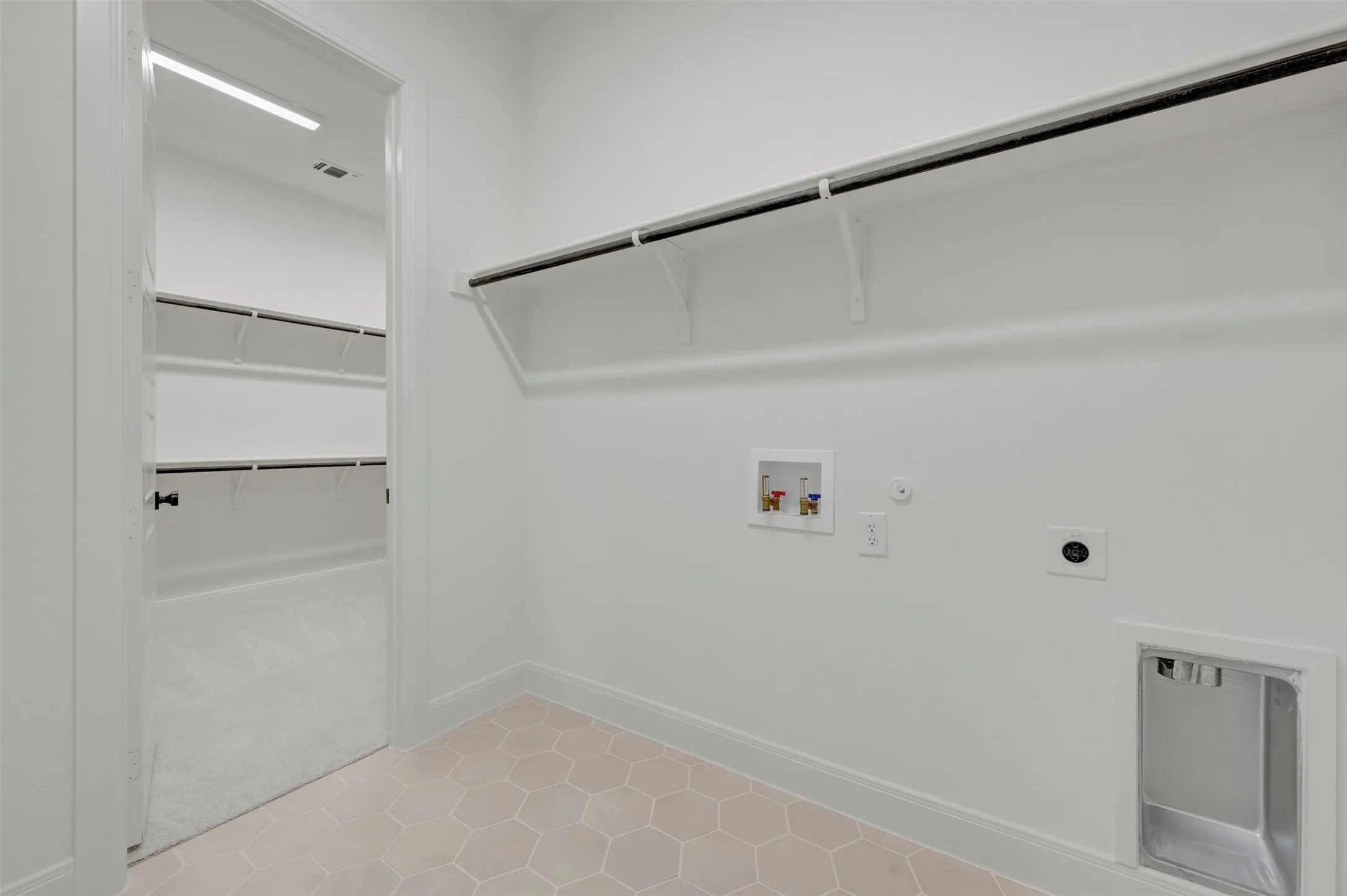 Laundry area featuring hexagonal tile flooring, a utility sink, and wall-mounted shelving with a clothing rod