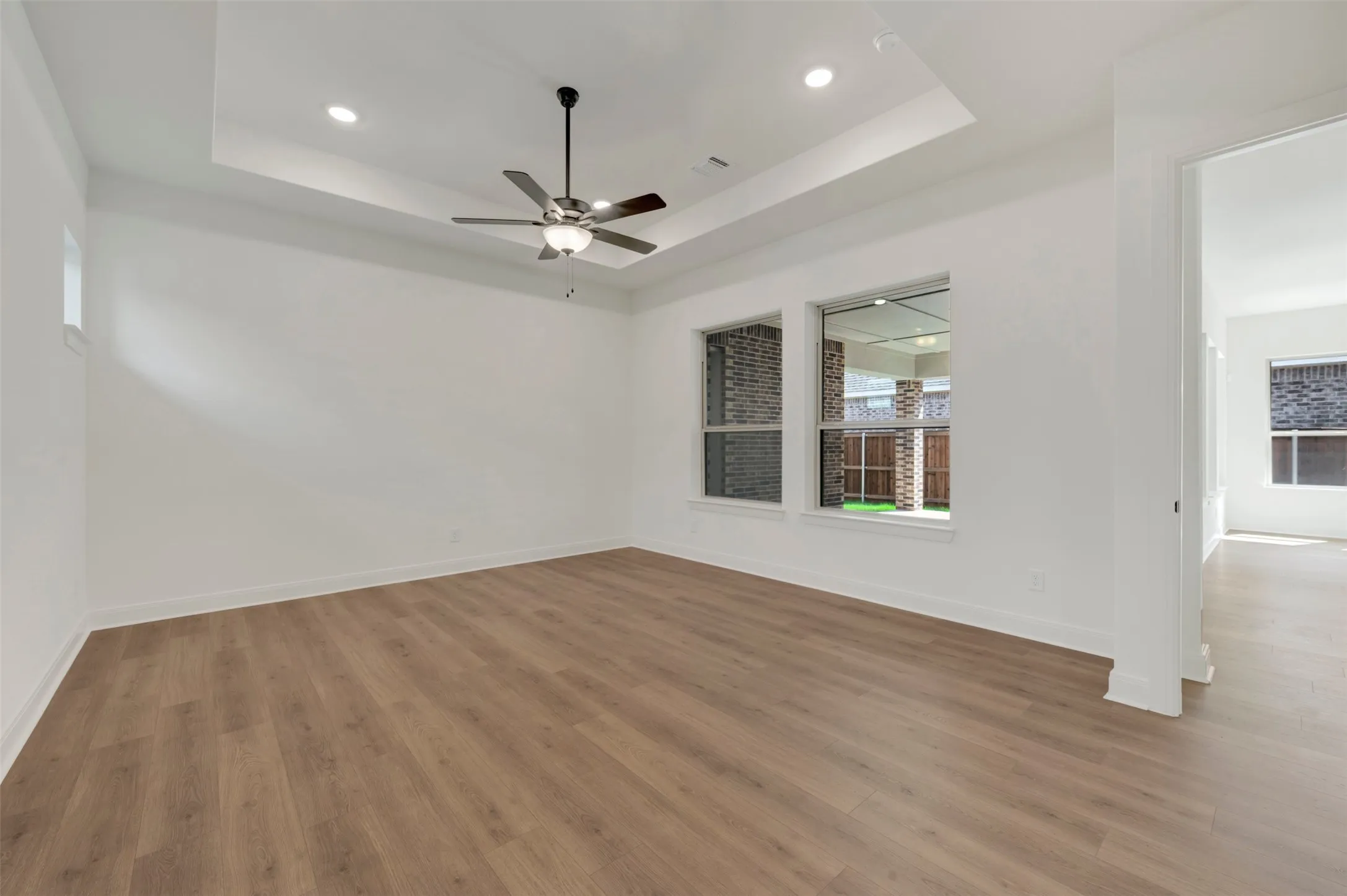 Spacious room featuring wood-finish flooring, a tray ceiling, recessed lighting, and a ceiling fan
