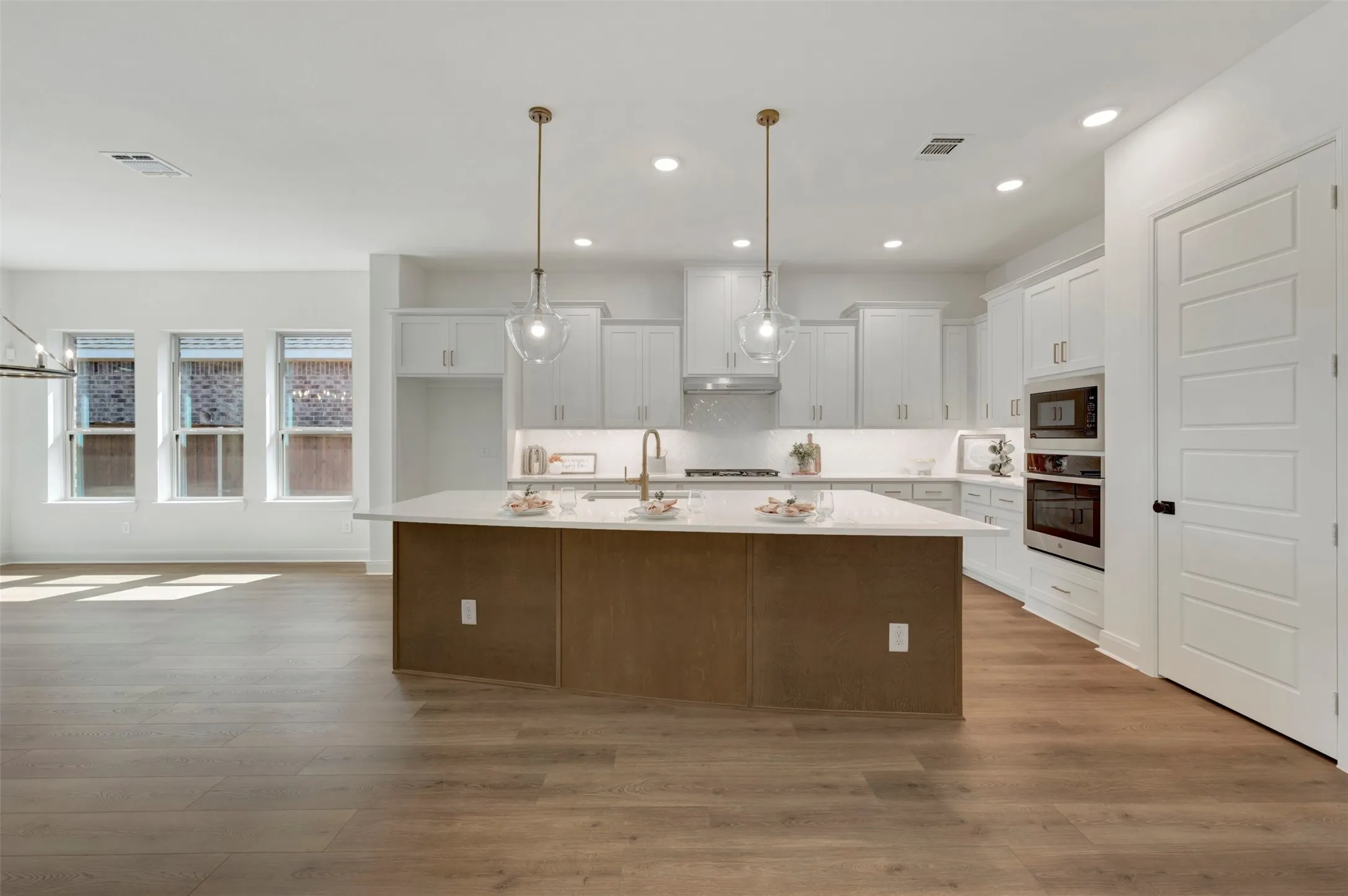 Open-concept kitchen featuring a large island with a light-toned countertop, white cabinetry, integrated stainless steel appliances, and wood-finish flooring