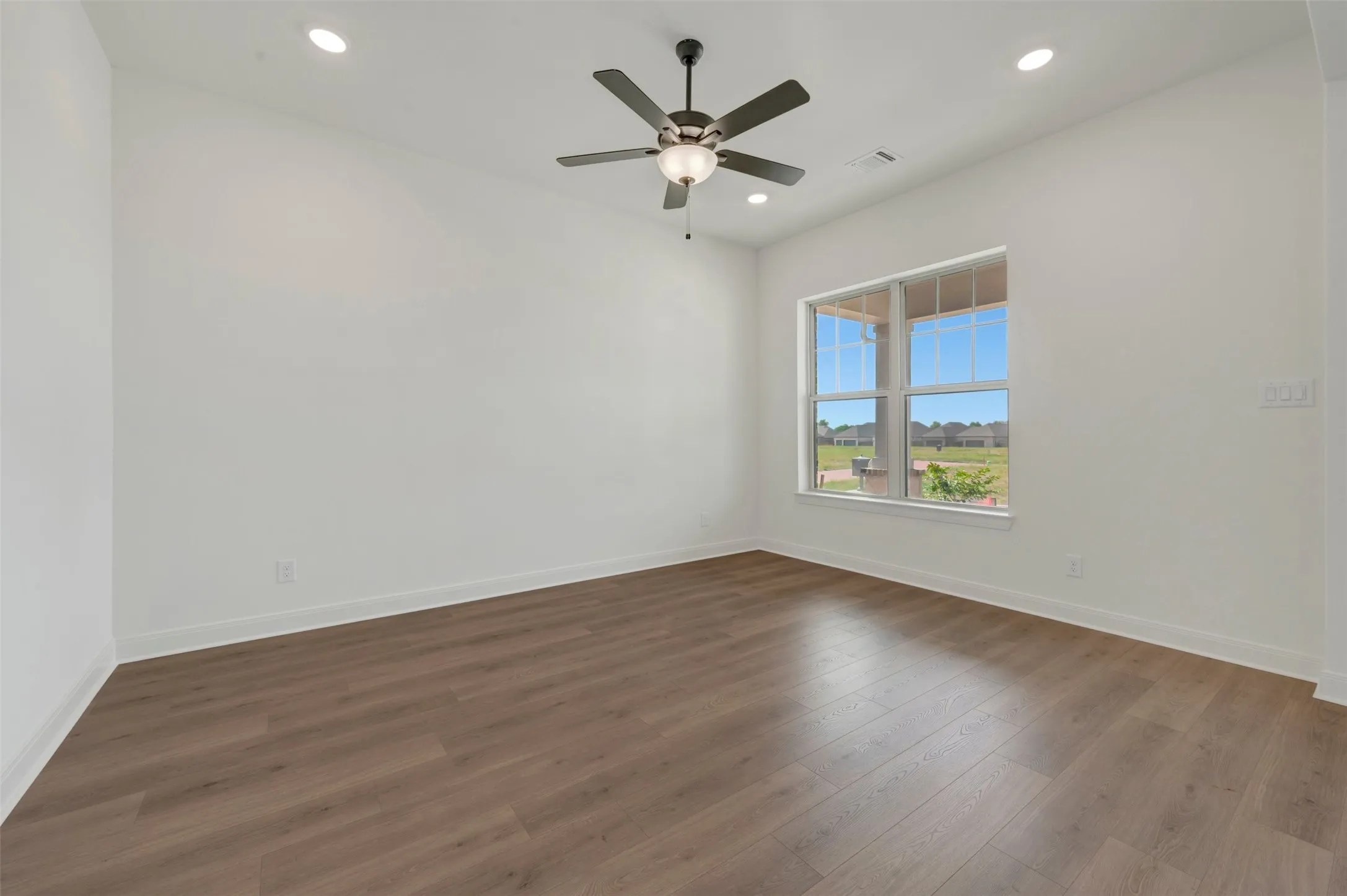 Room featuring wood-finish flooring, recessed lighting, a ceiling fan with light, and a large window overlooking the exterior