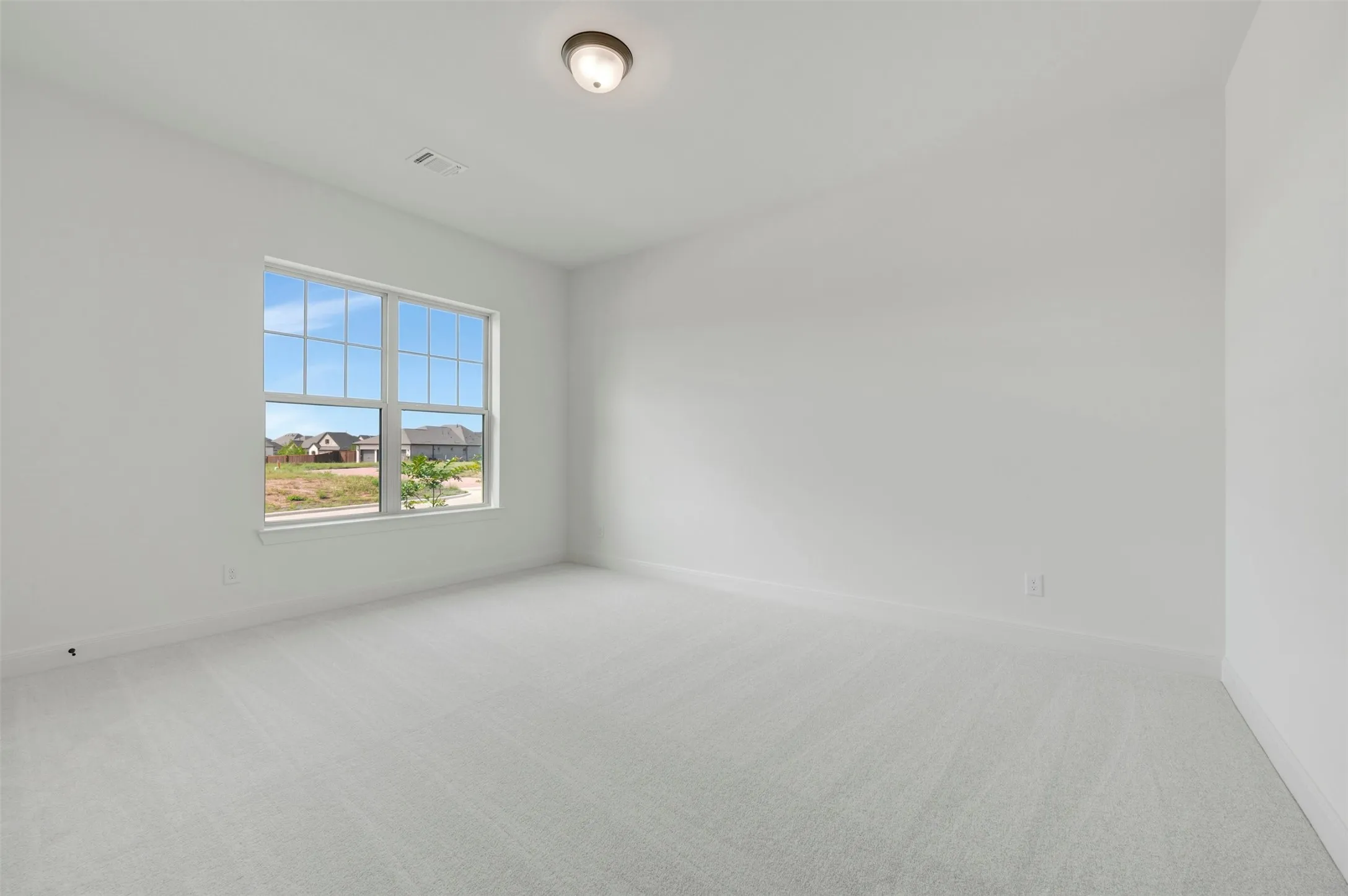 Bright interior room featuring a large window with grid panes, white walls, and light-colored carpet flooring