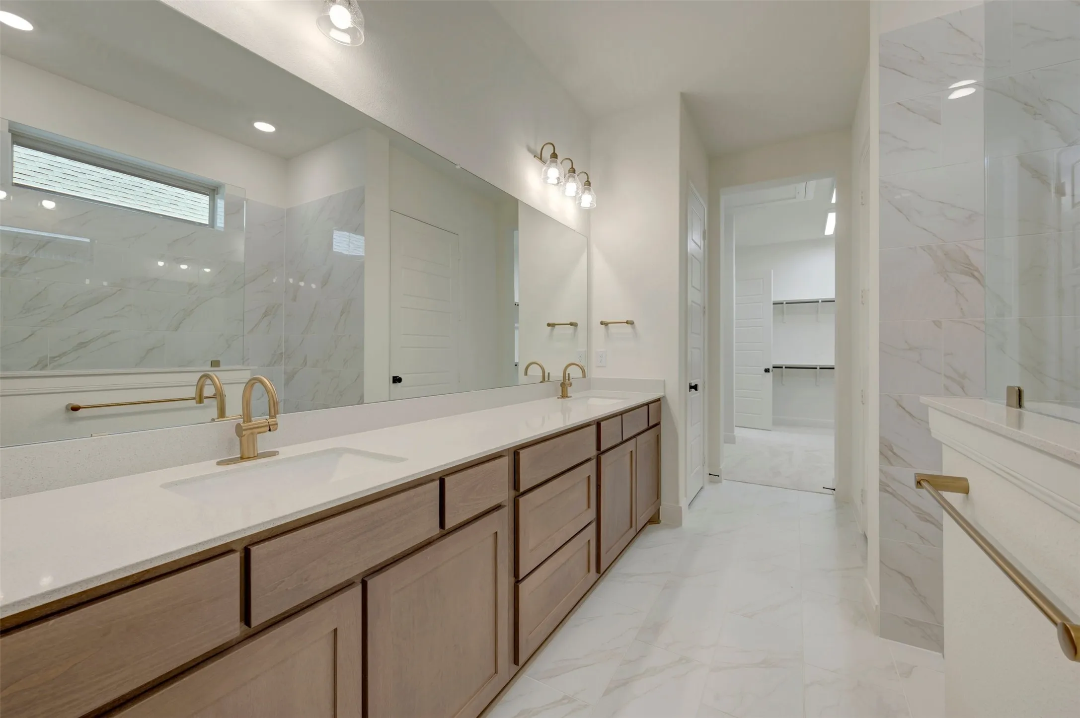 Double vanity with light wood-finish cabinetry, white countertops, and gold-tone fixtures