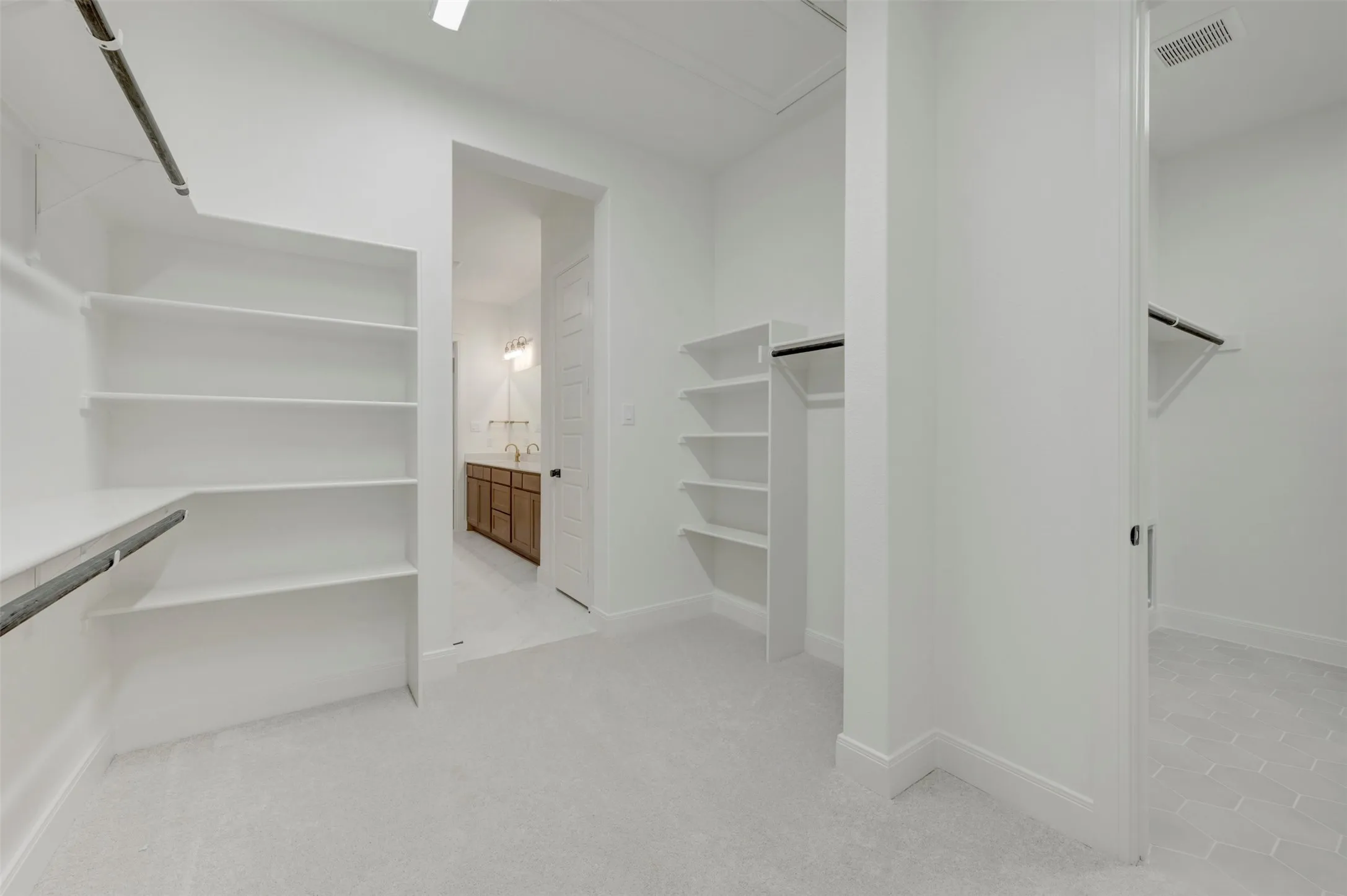 Spacious walk-in closet featuring extensive built-in shelving, hanging rods, and light gray carpet flooring