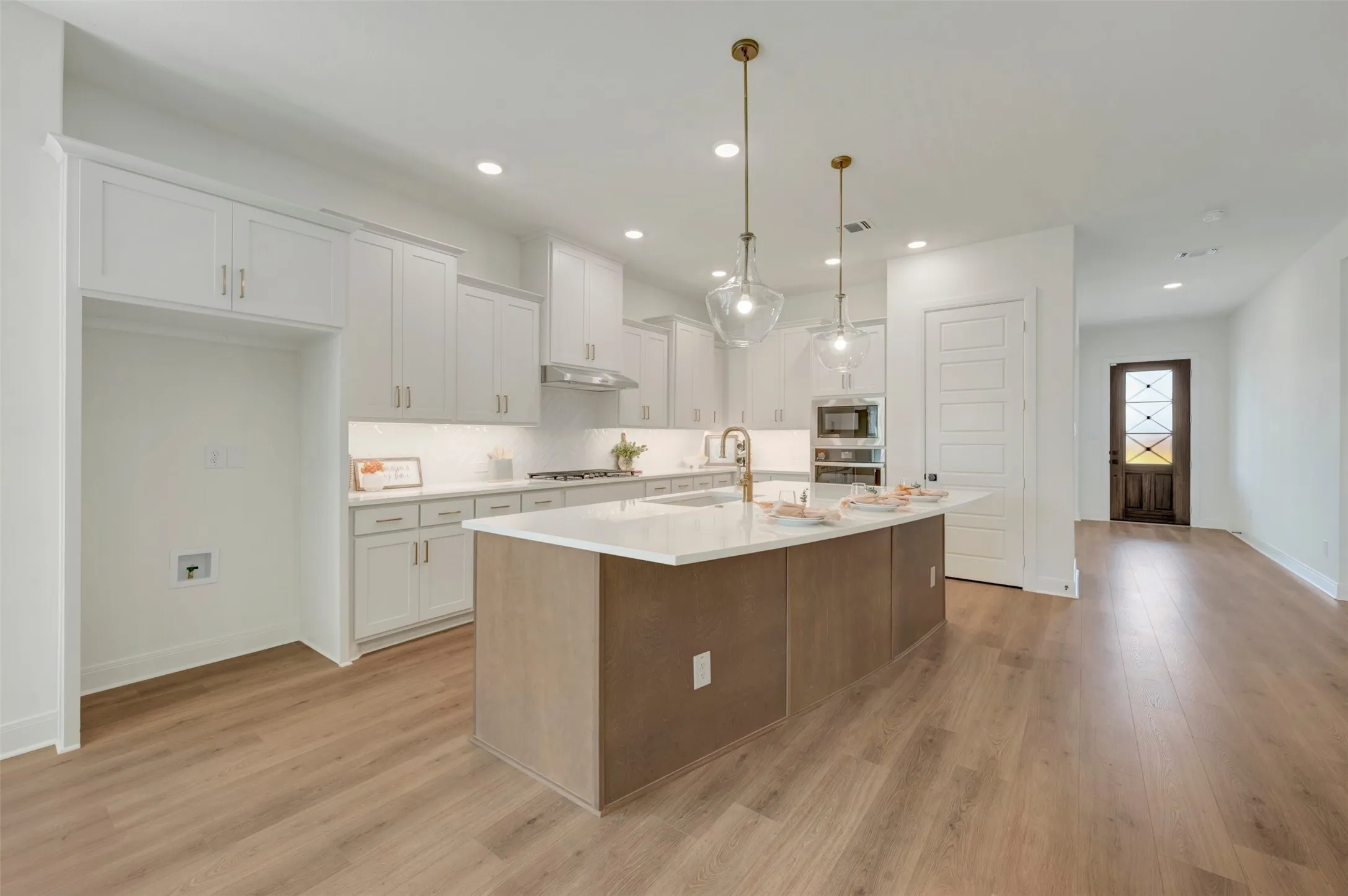 Modern kitchen featuring a large central island, white cabinetry, built-in appliances, and wood-finish flooring