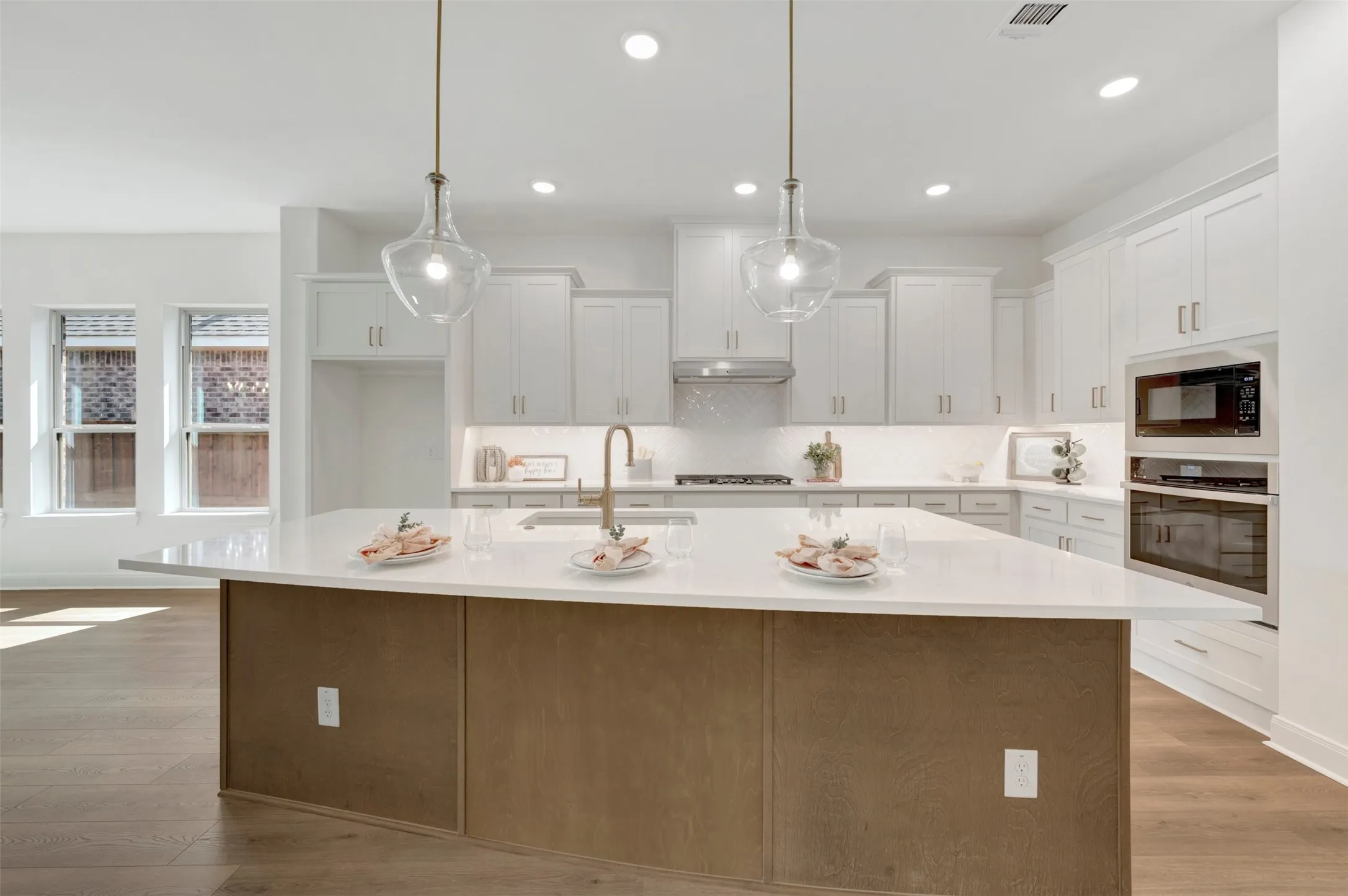 Modern kitchen featuring a large central island with a light-toned countertop and wood-finish paneling, under-cabinet lighting, ceiling-mounted recessed lighting, stainless steel appliances, and wood-finish flooring