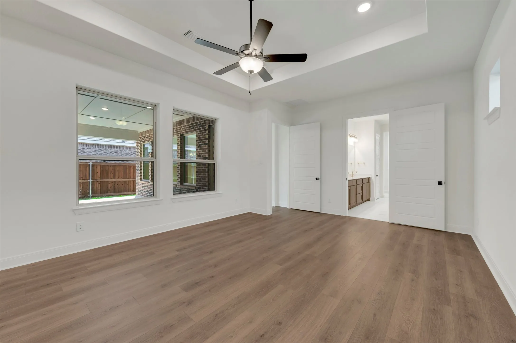 Spacious room featuring wood-finish flooring, a tray ceiling with a ceiling fan, and recessed lighting