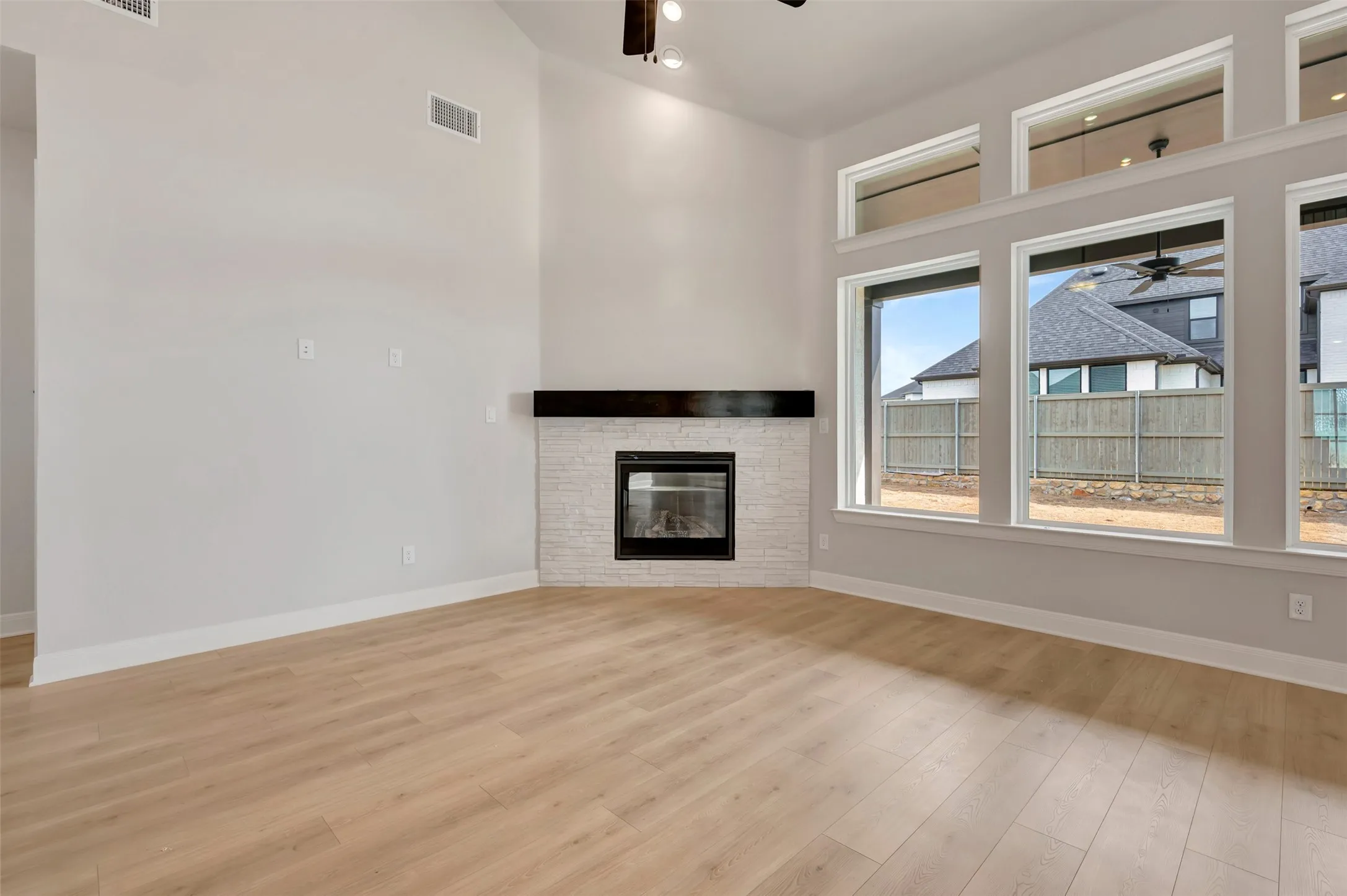 Unfurnished living room featuring ceiling fan, light wood finished floors, a stone fireplace, and a high ceiling