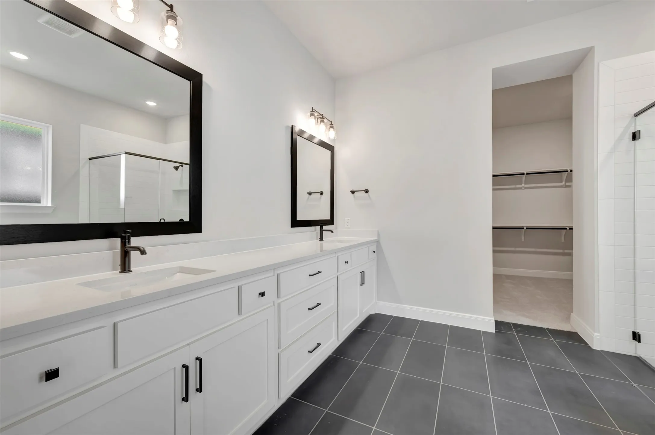 Bathroom featuring a stall shower, double vanity, a walk in closet, and dark tile patterned floors