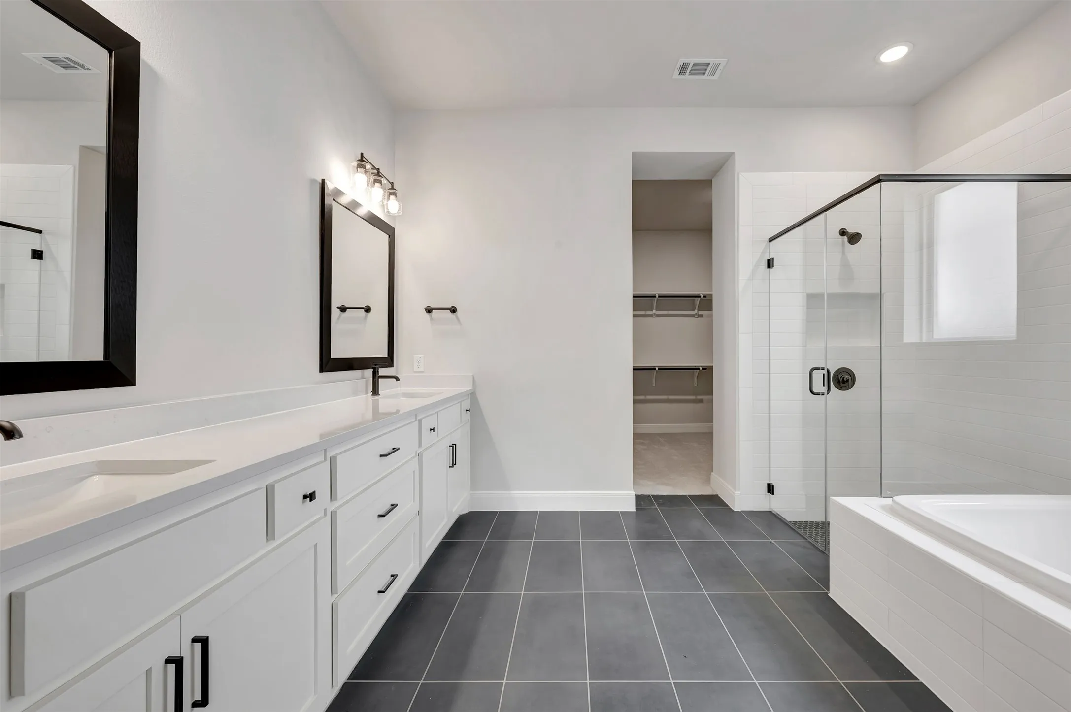 Bathroom featuring a shower stall, double vanity, dark tile patterned flooring, a bath, and a walk in closet