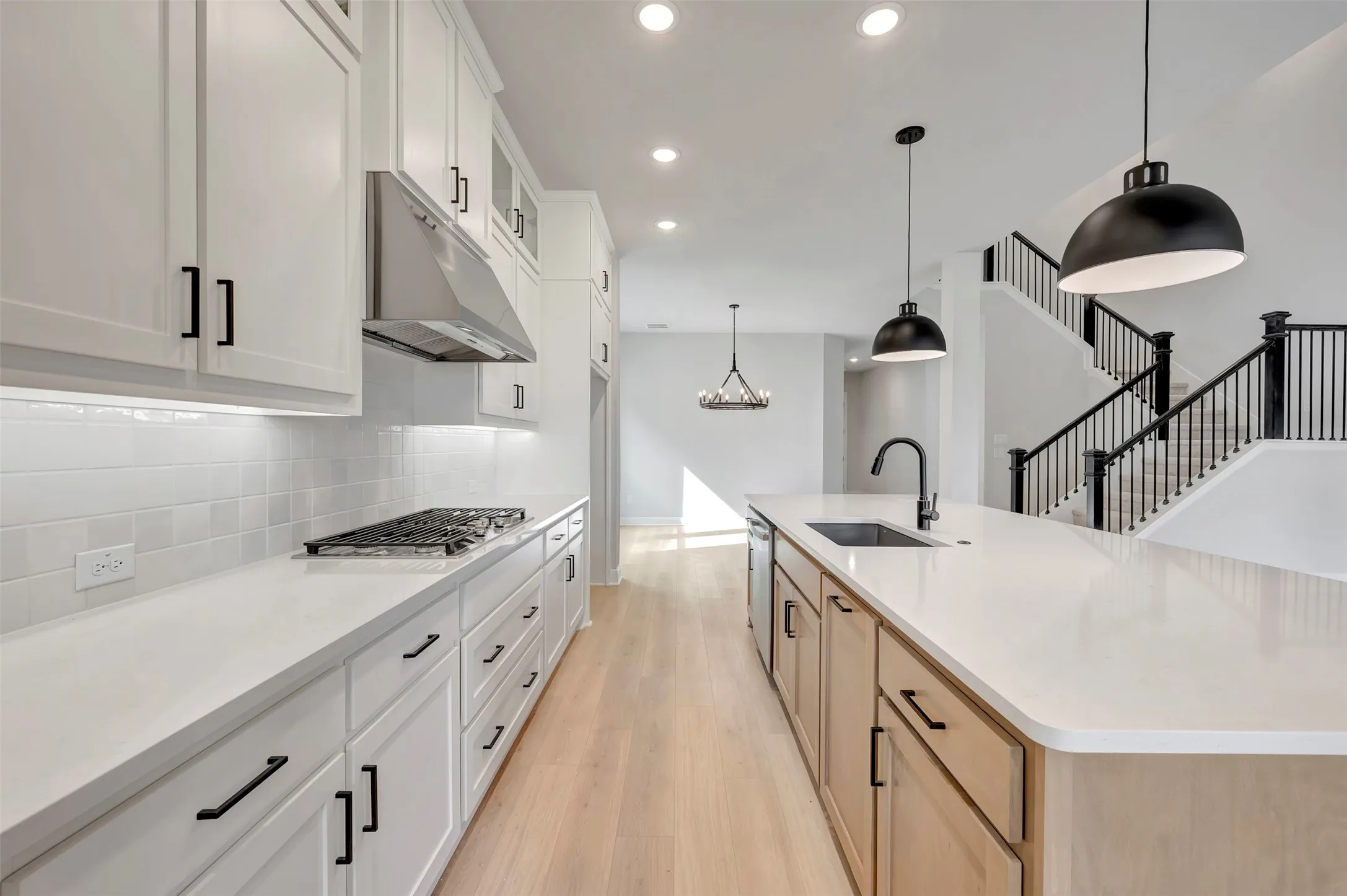 Two tone kitchen featuring two tone cabinets, light wood-type flooring, a large island with sink, hanging light fixtures, and decorative backsplash
