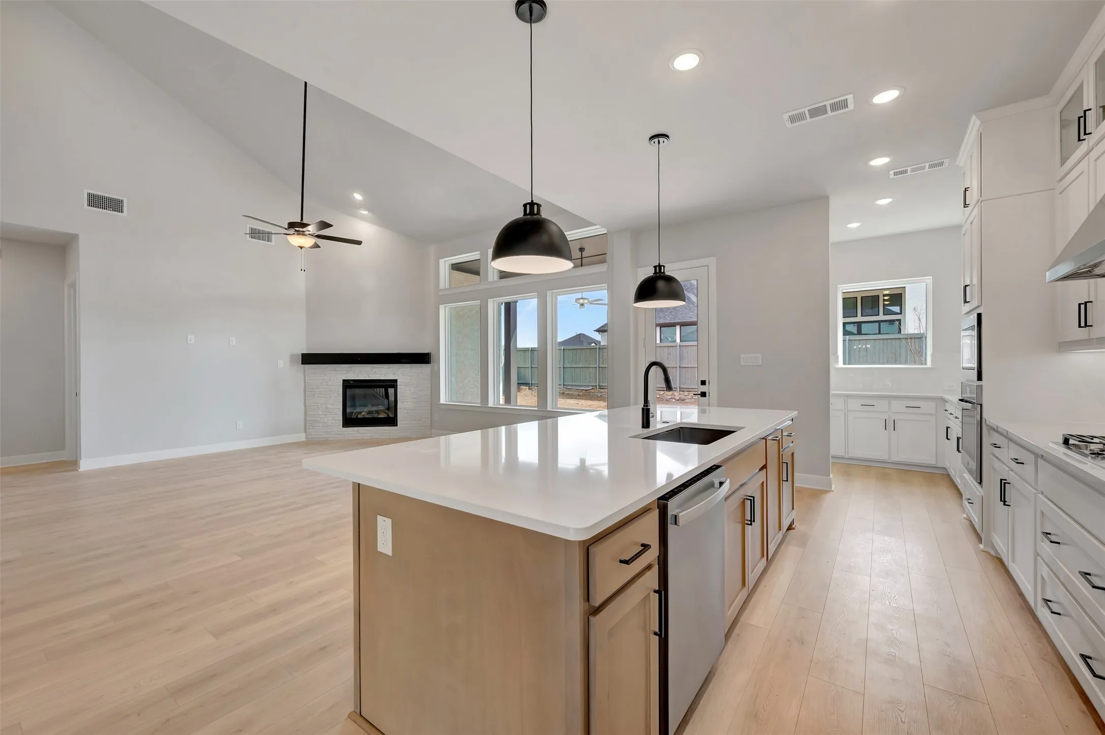 Dual tone kitchen with a glass covered fireplace, pendant lighting, light wood-type flooring, an island with sink, and stainless steel appliances