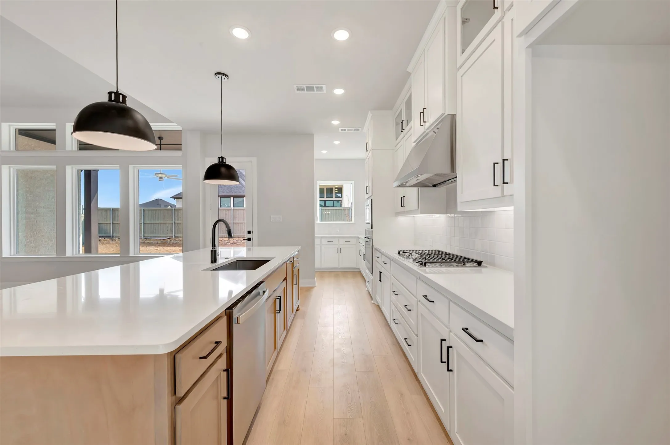 Kitchen with light wood-type flooring, hanging light fixtures, white cabinets, a large island, and stainless steel appliances