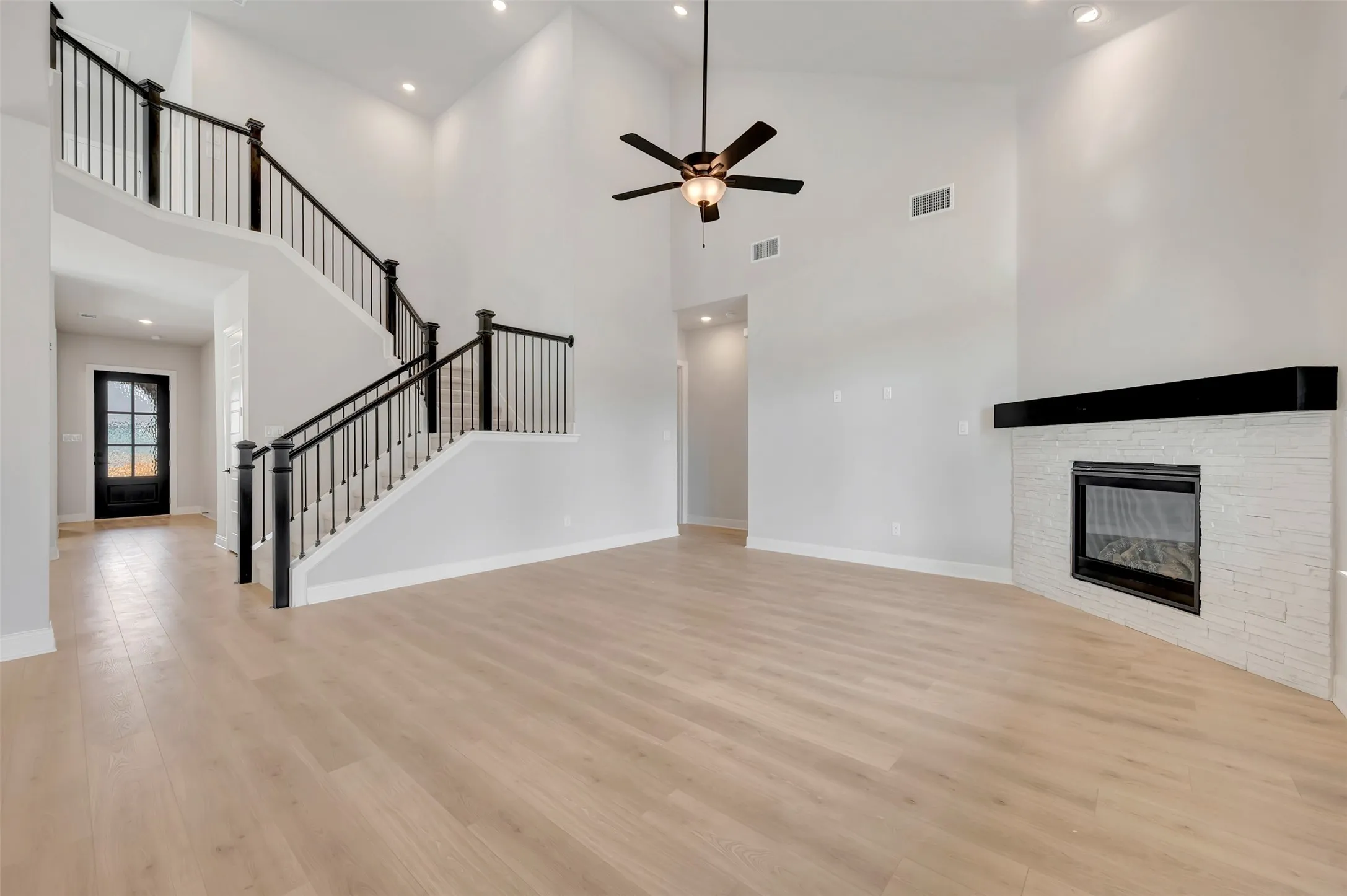 Unfurnished living room featuring a fireplace, ceiling fan, recessed lighting, light wood-style flooring, and a high ceiling