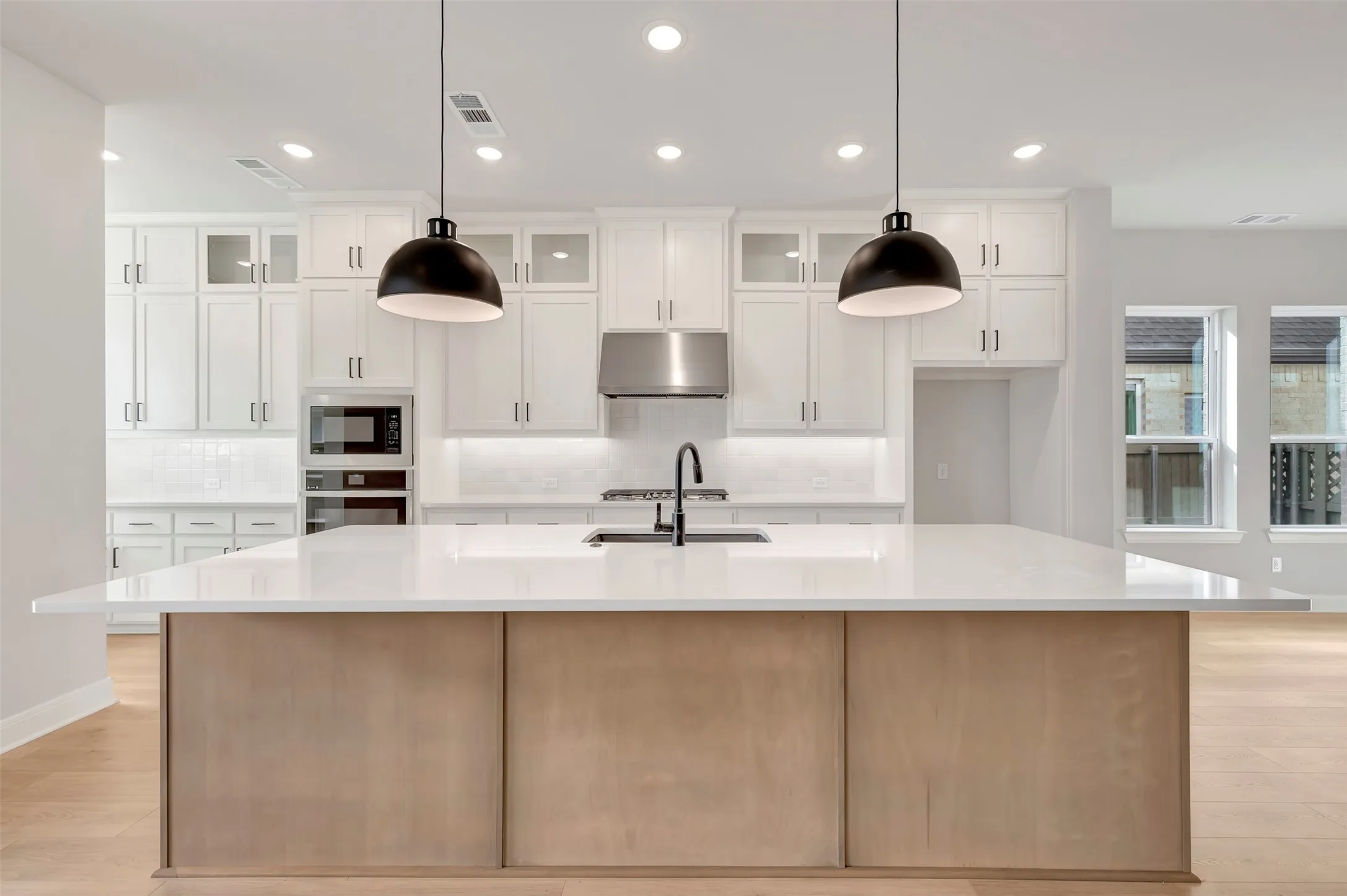 Kitchen with light wood finished floors, glass insert cabinets, a spacious island, tasteful backsplash, and two tone cabinets