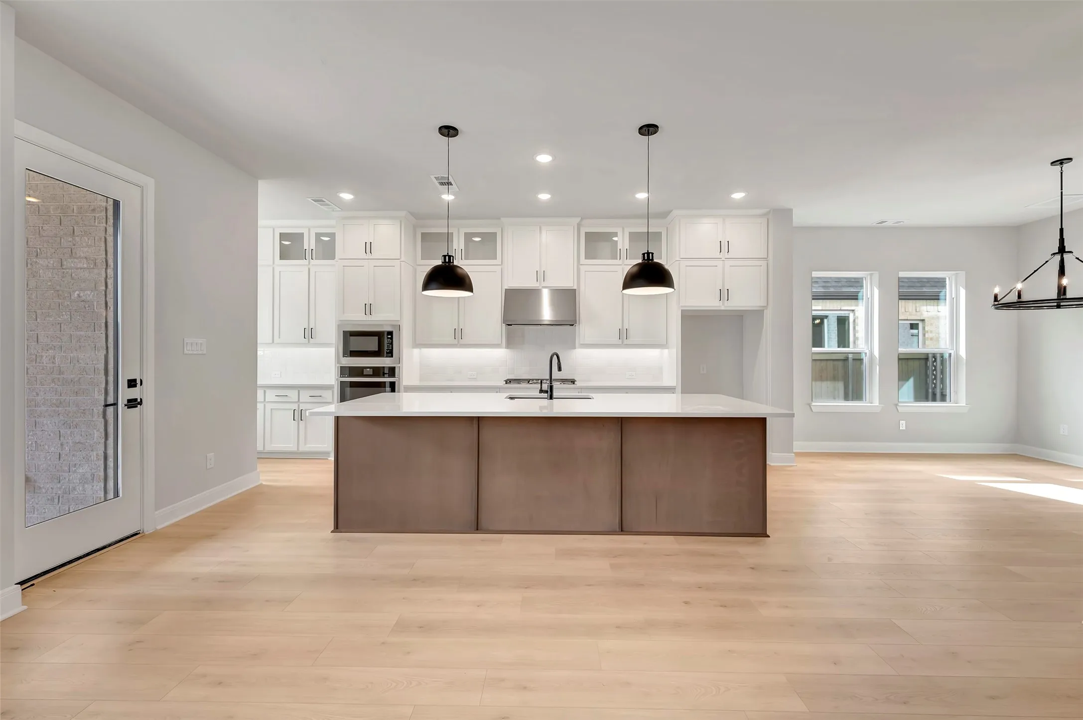 Dual tone kitchen featuring a large island with sink, glass fronted cabinets, light wood-style flooring, dual tone cabinetry, and stainless steel appliances