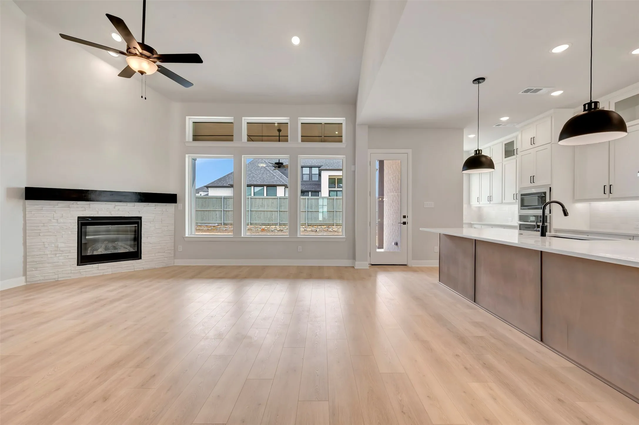 Kitchen with dual tone cabinetry, ceiling fan, a stone fireplace, open floor plan, and light wood-type flooring