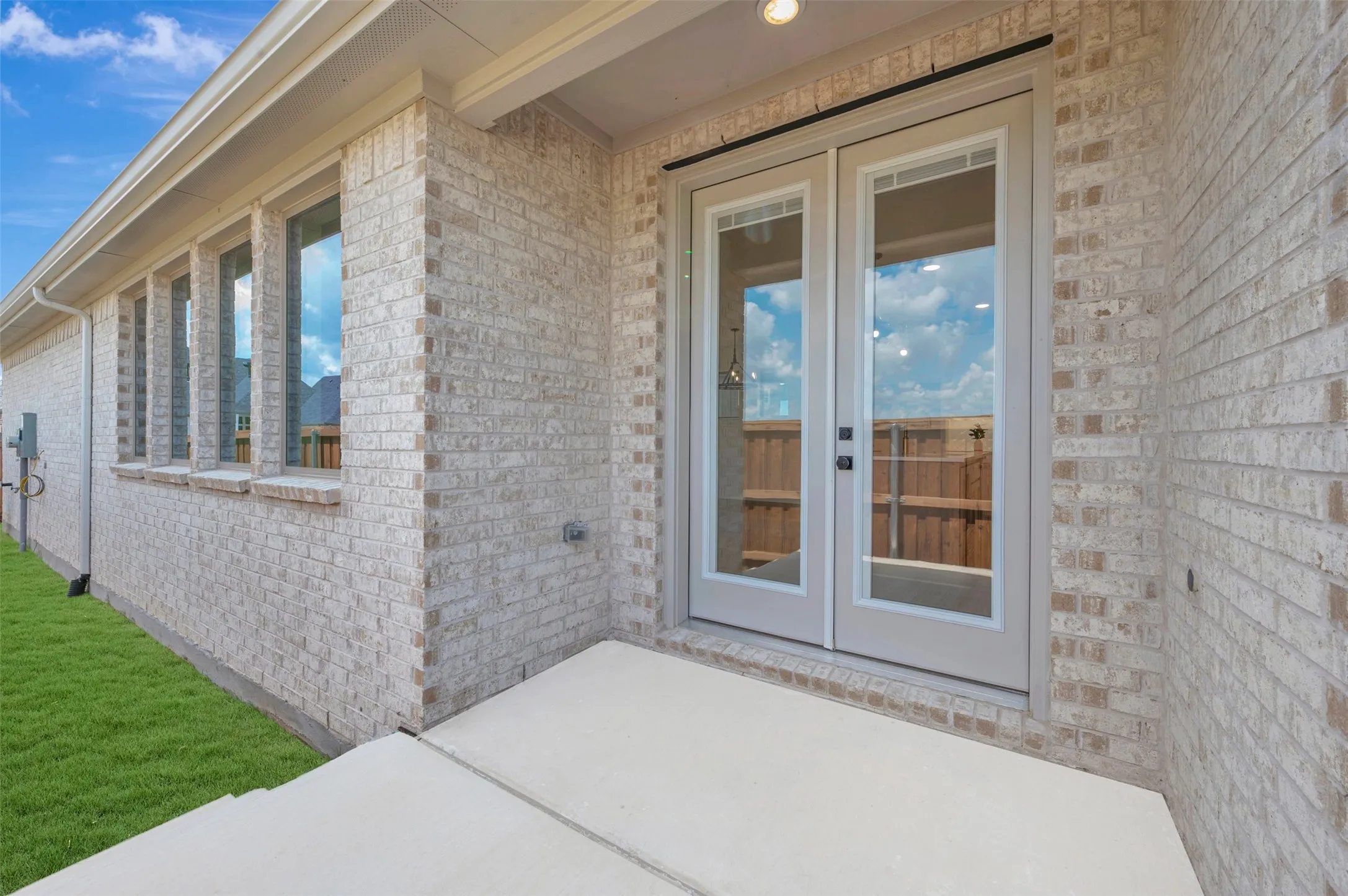 Expansive concrete patio with double glass-paneled French doors and a light brick facade