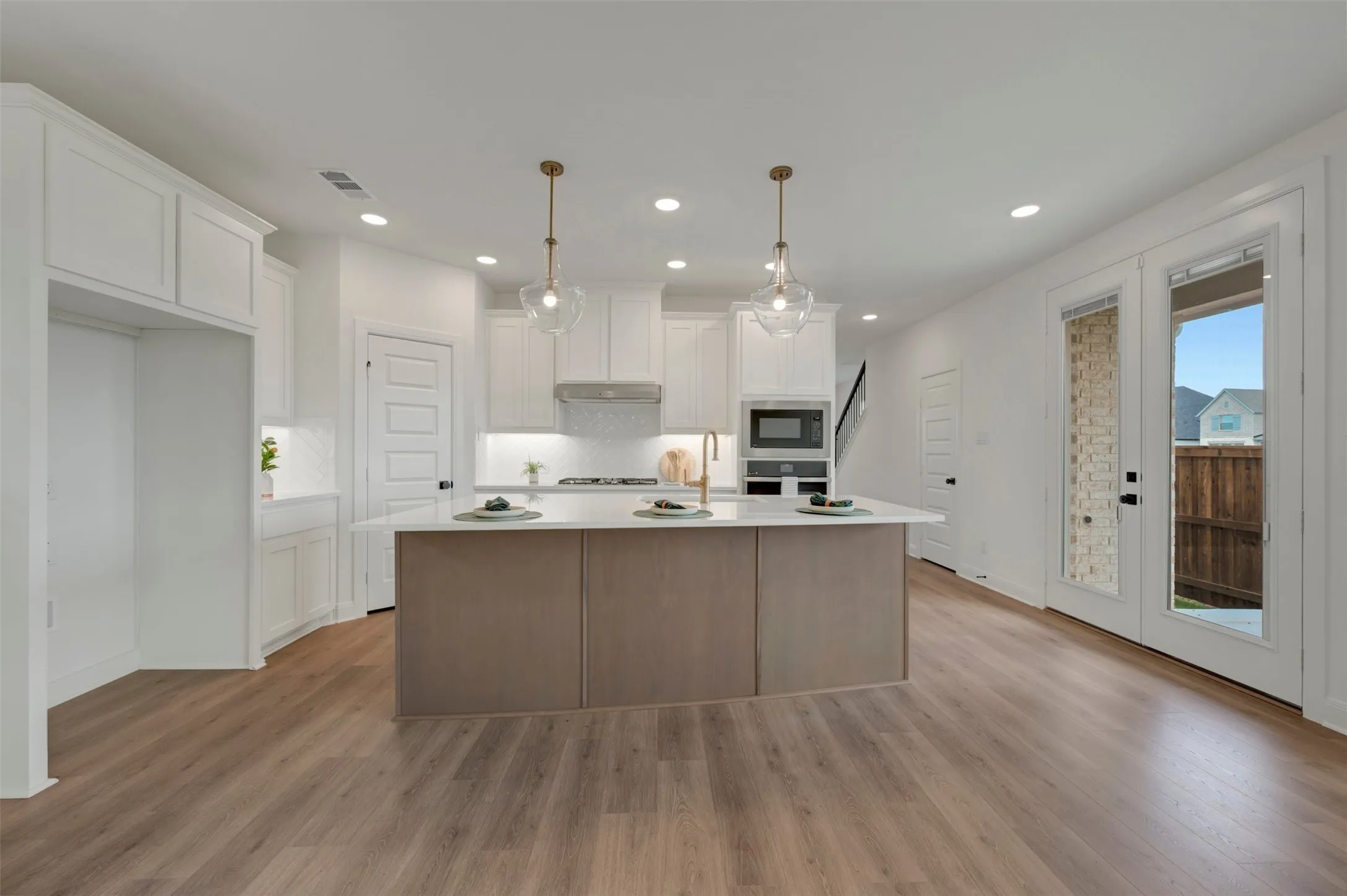 Contemporary kitchen featuring a large central island with a light-toned countertop, white cabinetry with crown molding, integrated microwave, and wood-finish flooring