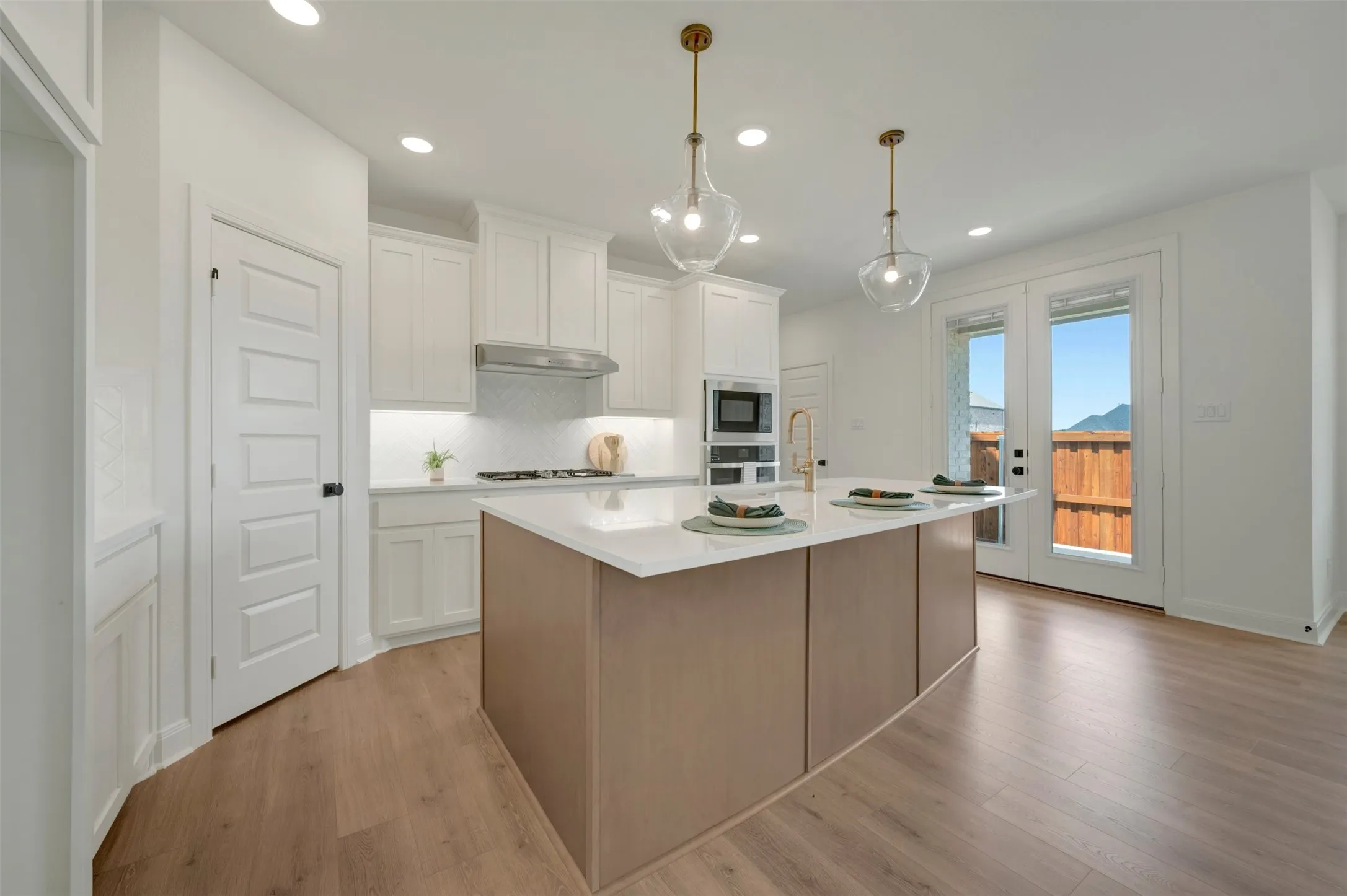 Modern kitchen featuring a central island with a light-toned base, white countertop, and two glass pendant lights