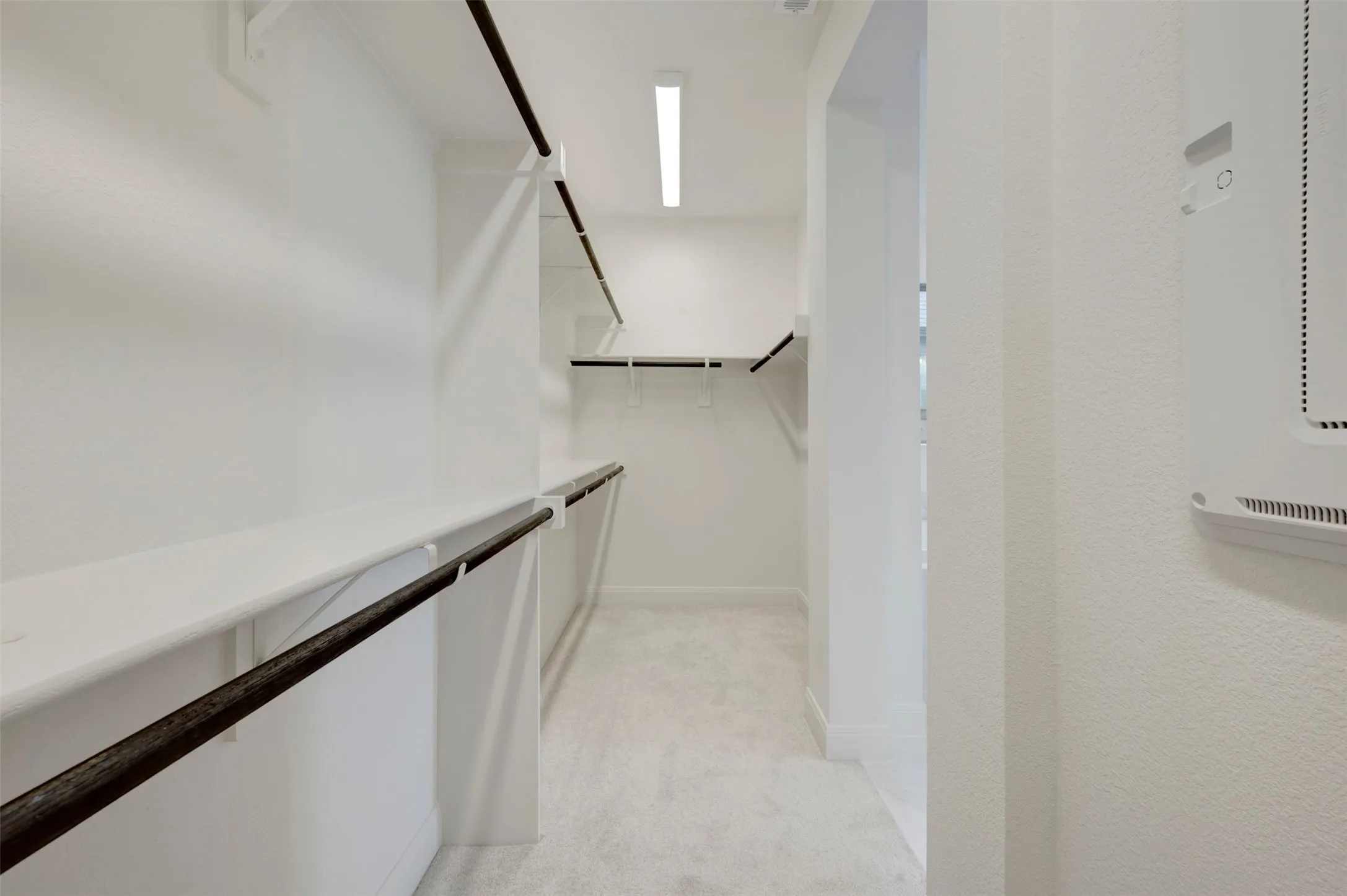 Walk-in closet featuring white wall shelving and dark-finished hanging rods, recessed overhead lighting, and light-toned carpeting
