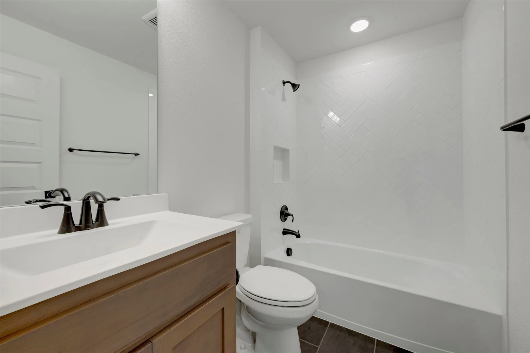 Bathroom featuring a dark wood-finish vanity, white countertop, black fixtures, a white subway tile shower surround, and dark tile flooring
