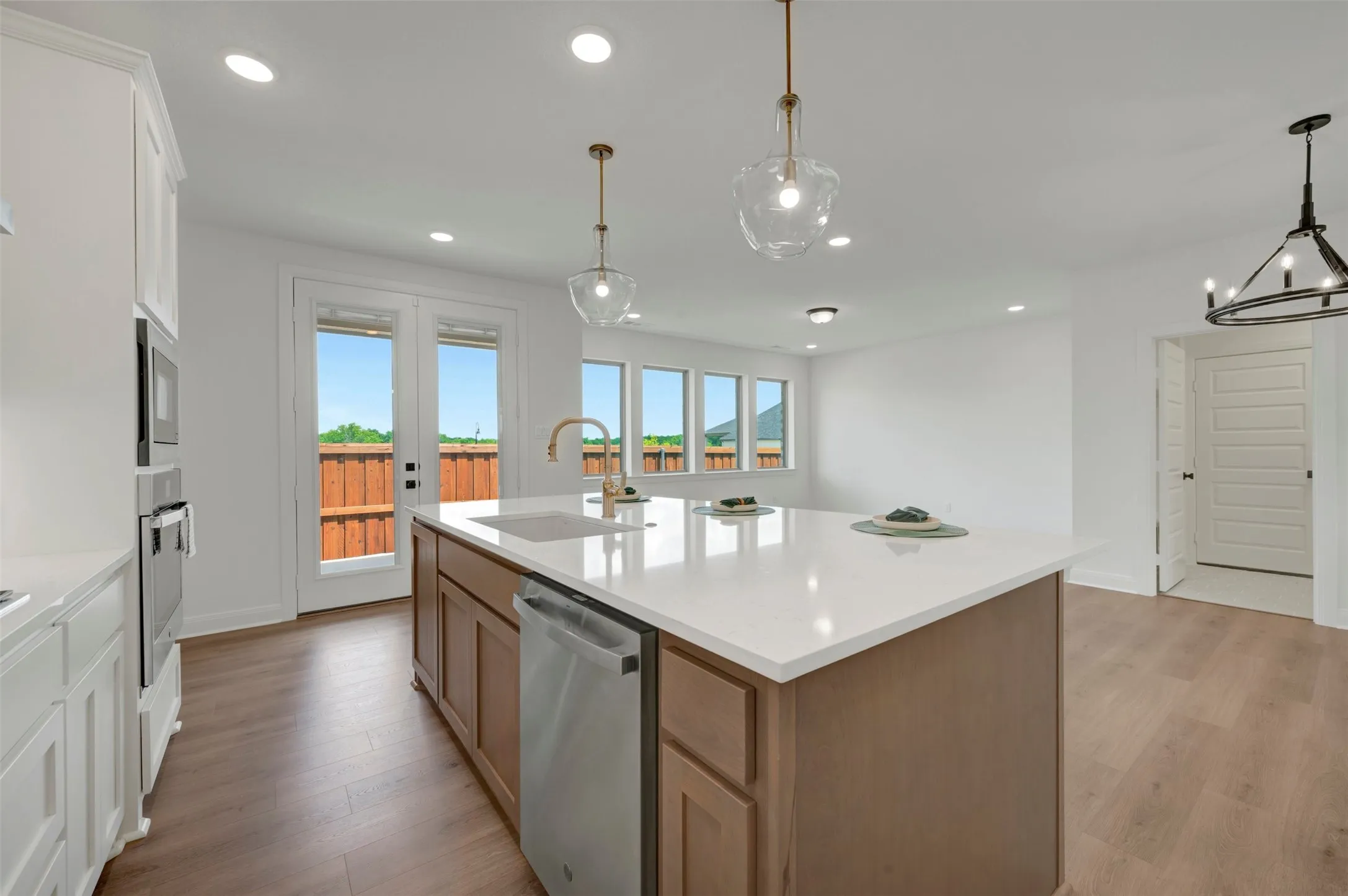 Contemporary kitchen island featuring a white countertop, undermount sink with brass-finish faucet, integrated dishwasher, and clear glass pendant lighting
