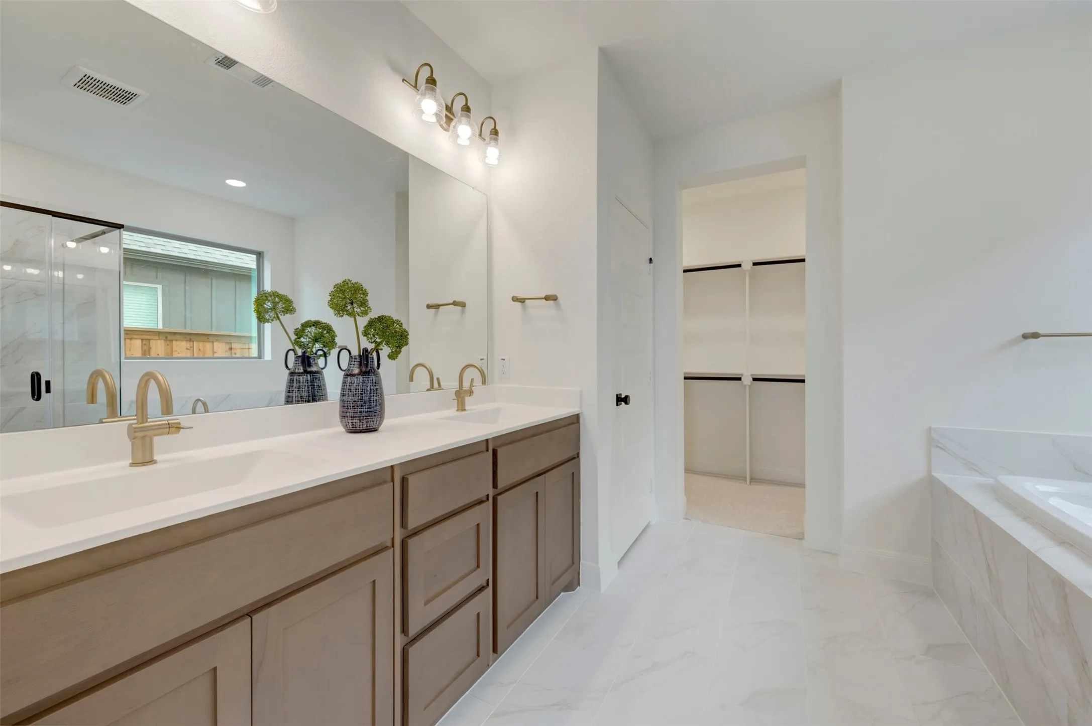 Dual vanity with brushed gold fixtures, white countertops, and wood-finish cabinetry
