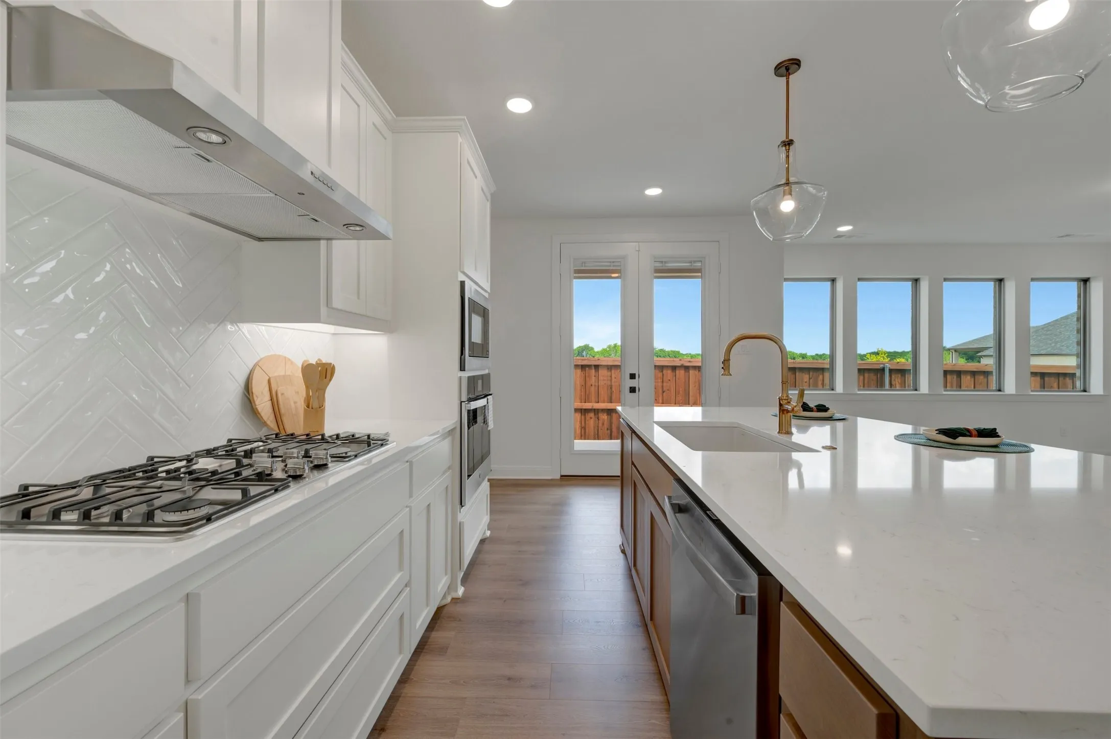 Modern kitchen featuring white cabinetry, a gas cooktop, herringbone tile backsplash, and stainless steel appliances