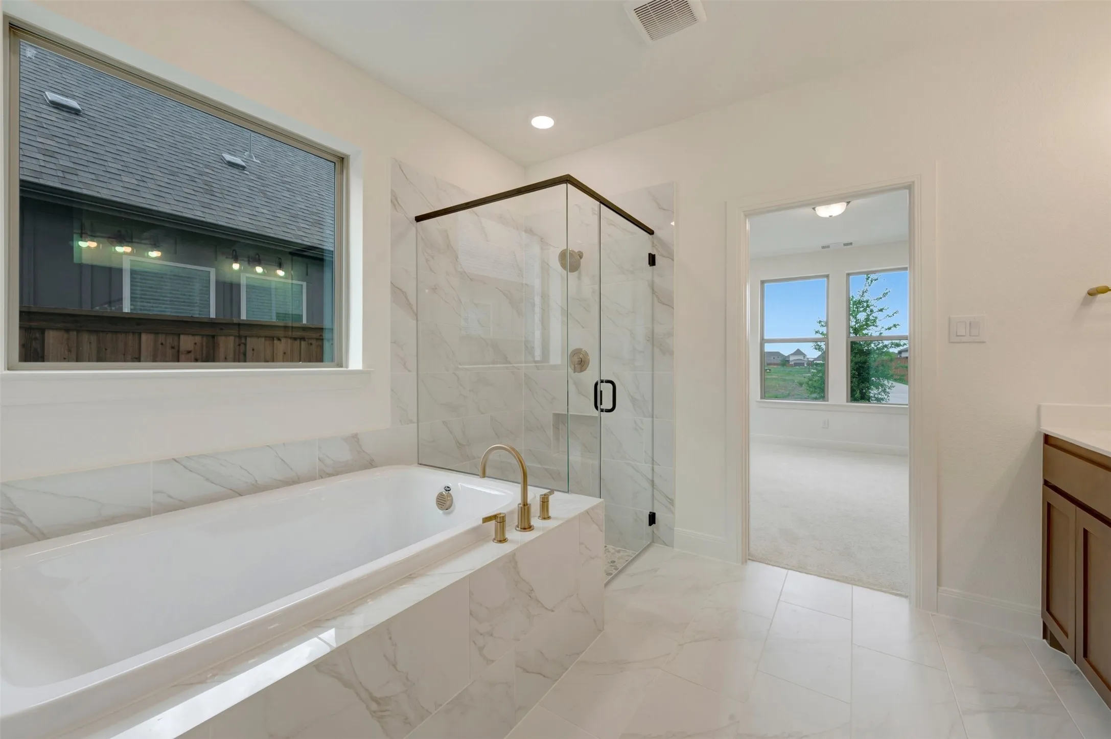 Contemporary bathroom featuring a built-in soaking tub with gold-finish fixtures, a glass-enclosed shower with marble-look tile surround, and white tile flooring