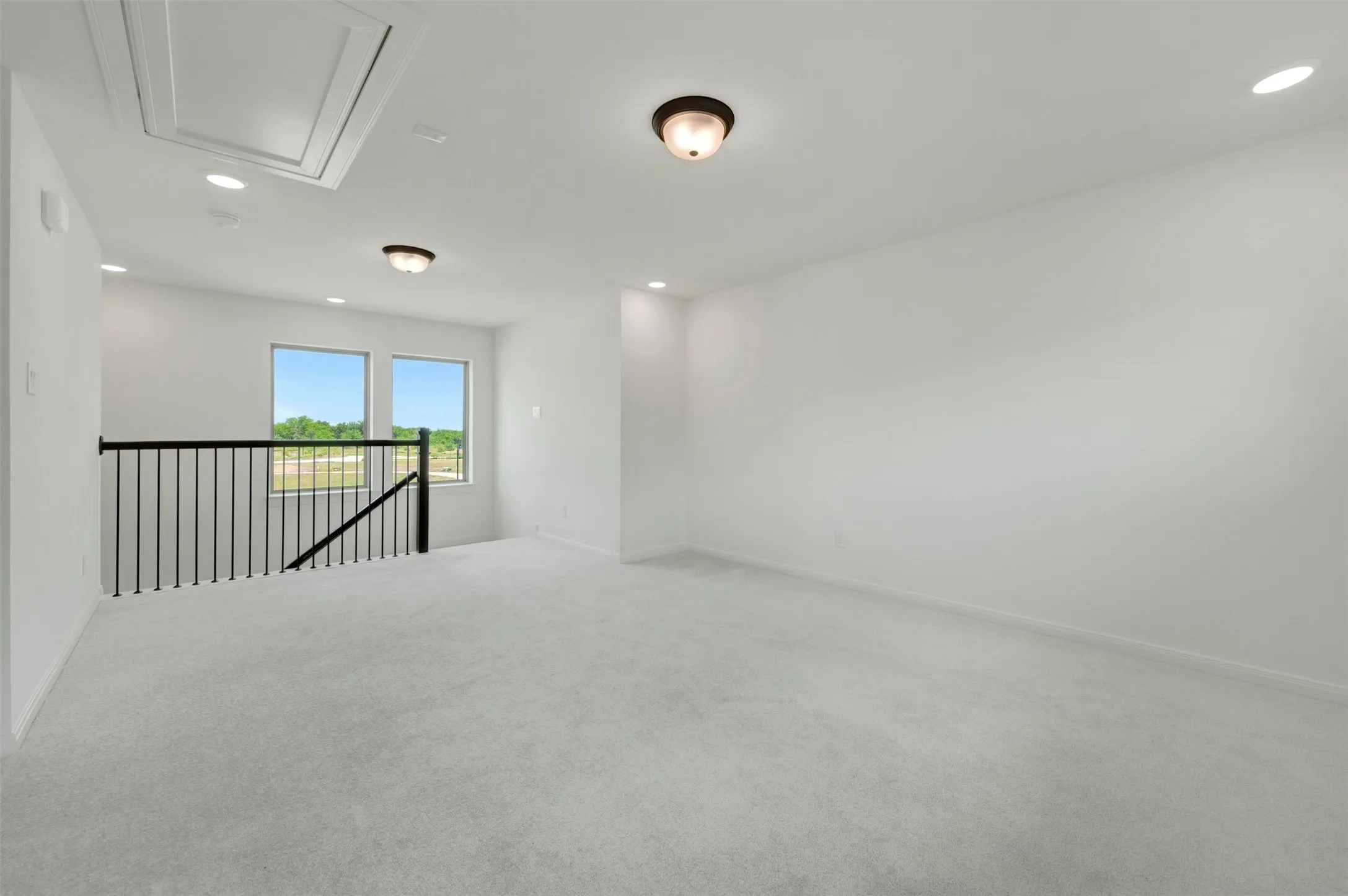 Spacious carpeted room featuring a black metal railing, two windows, recessed lighting, and a ceiling-mounted light fixture