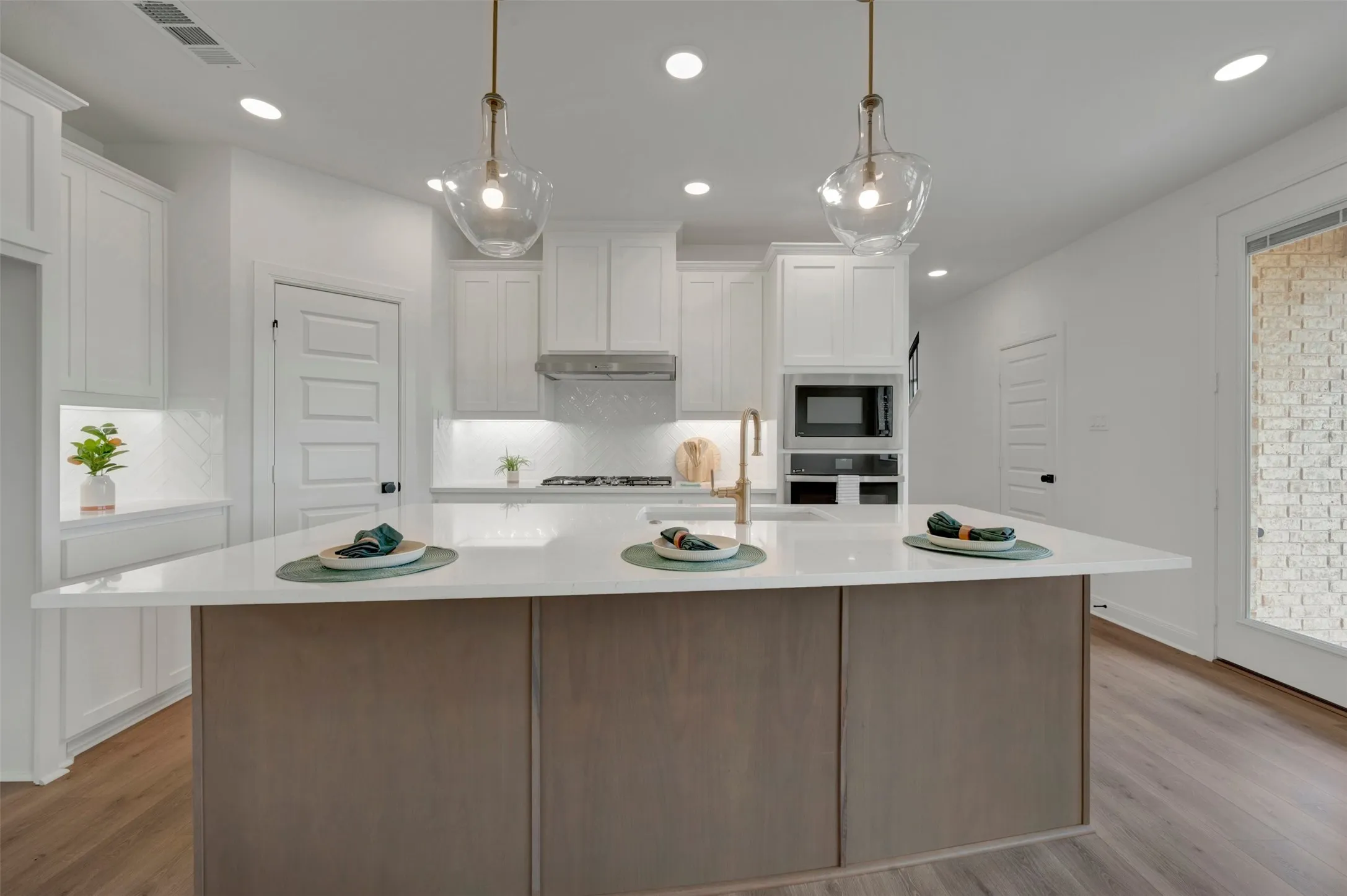 Central kitchen island with a light-toned countertop and wood-finish paneling, complemented by two glass pendant lights