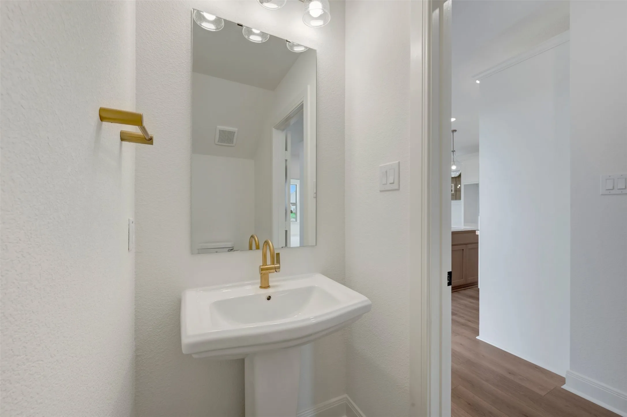 Pedestal sink featuring a gold-finish faucet, framed mirror, and coordinating gold-finish towel bar