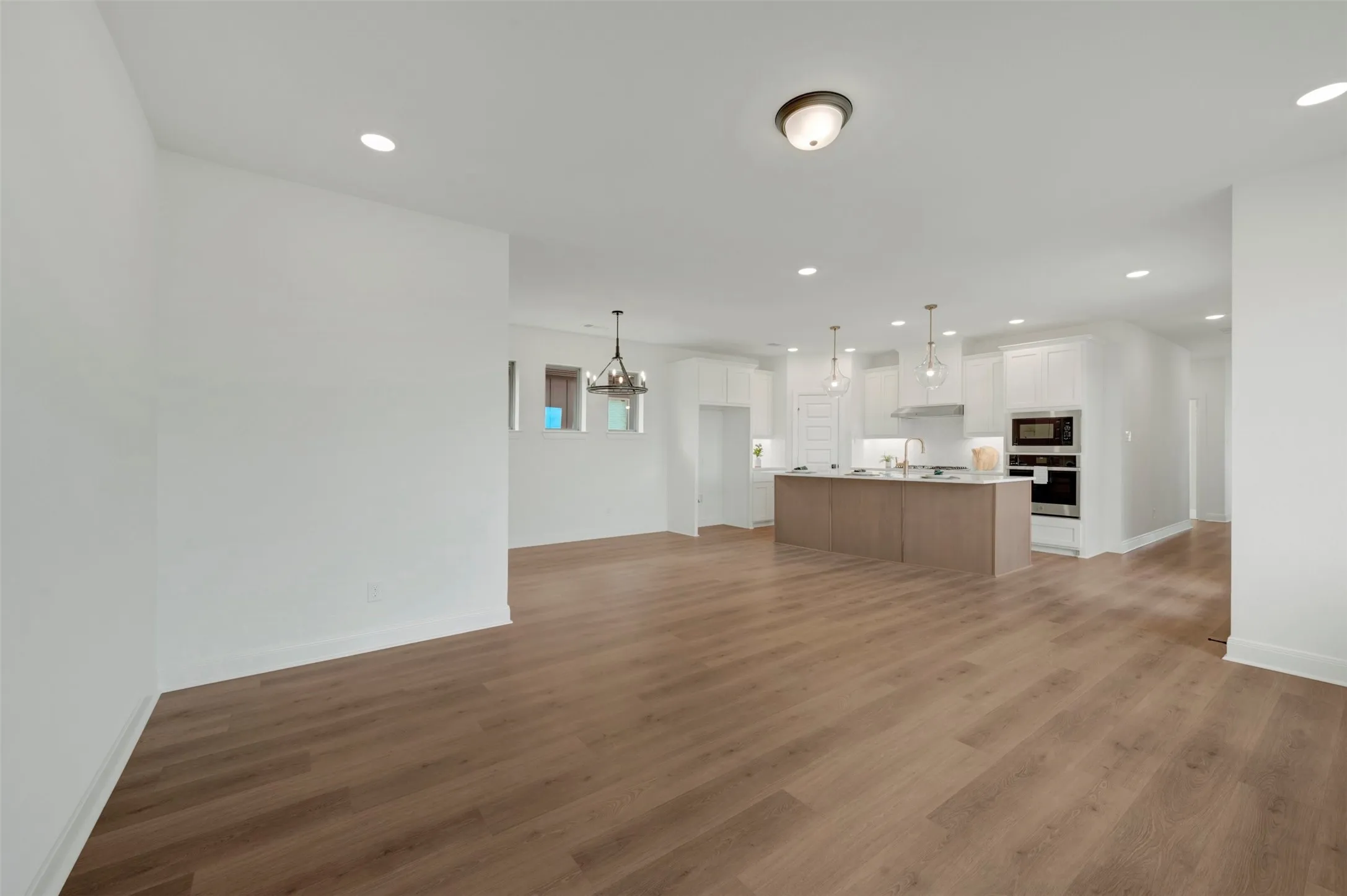 Open-concept living area featuring wood-finish flooring, recessed lighting, and a kitchen with white cabinetry, a central island, and stainless steel appliances